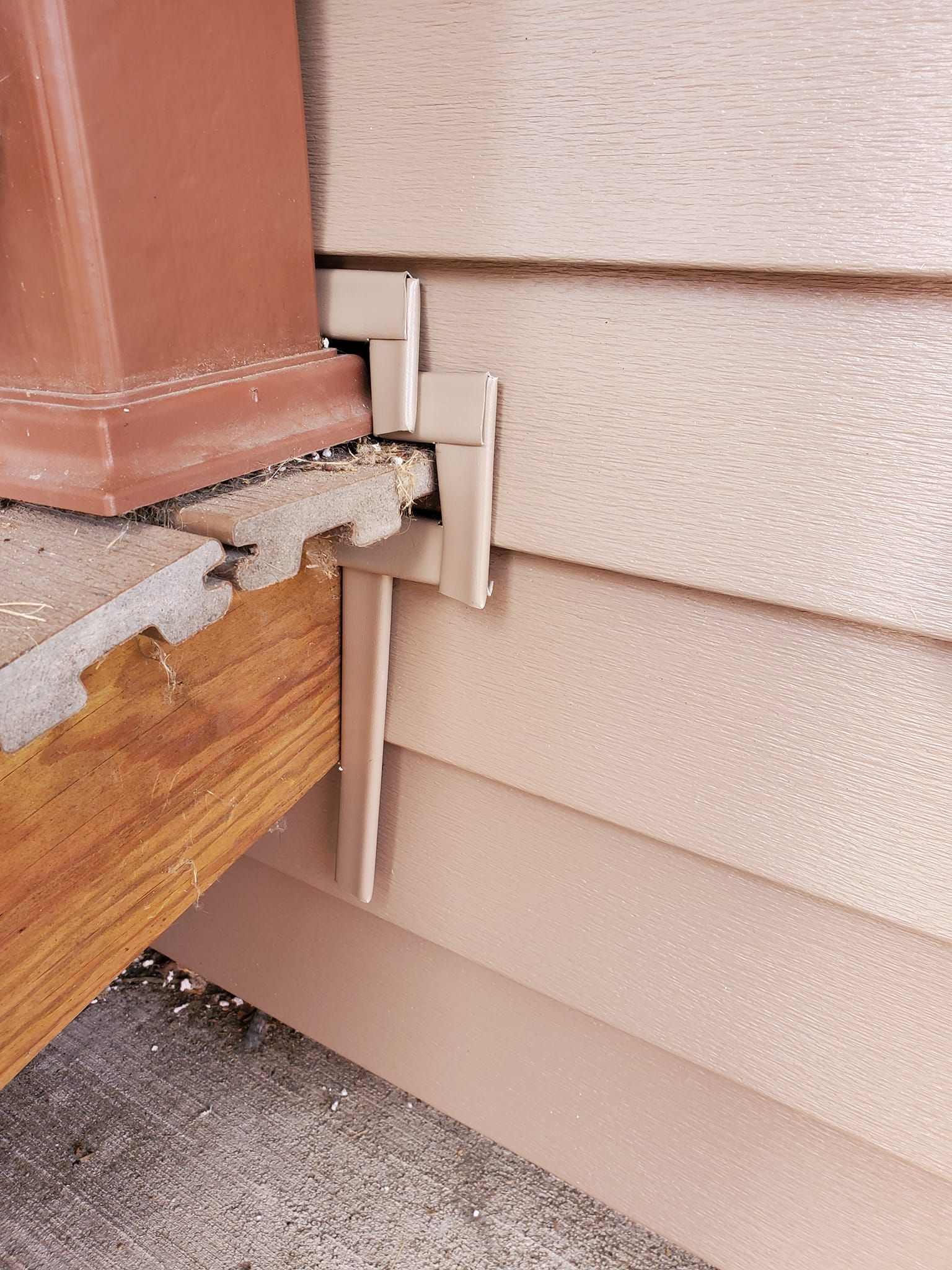 Close-up of damaged house siding with a cracked trim joint and exposed wood near the foundation.