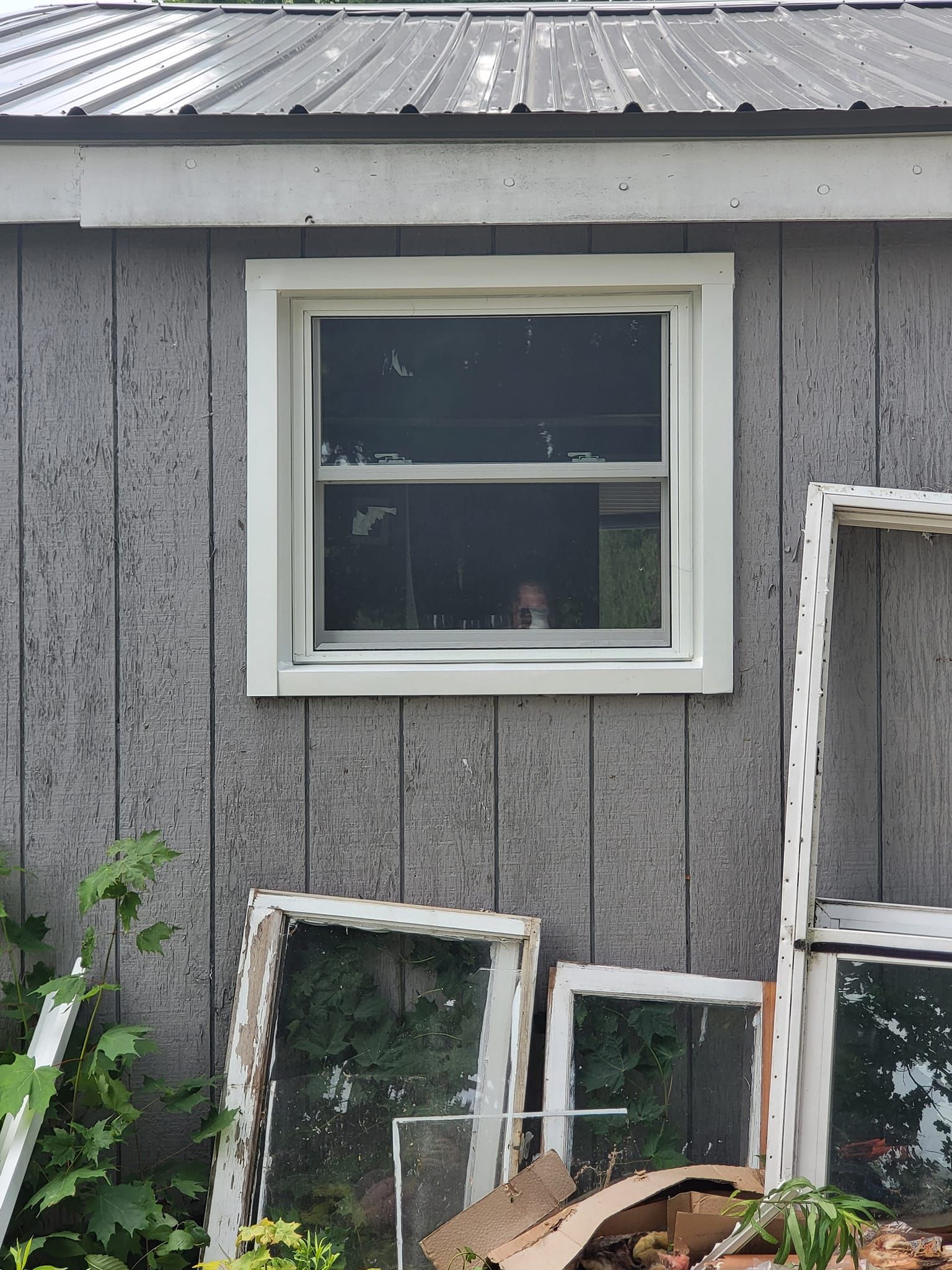 Gray weathered house wall with a white-framed window and several old window panes leaning below it