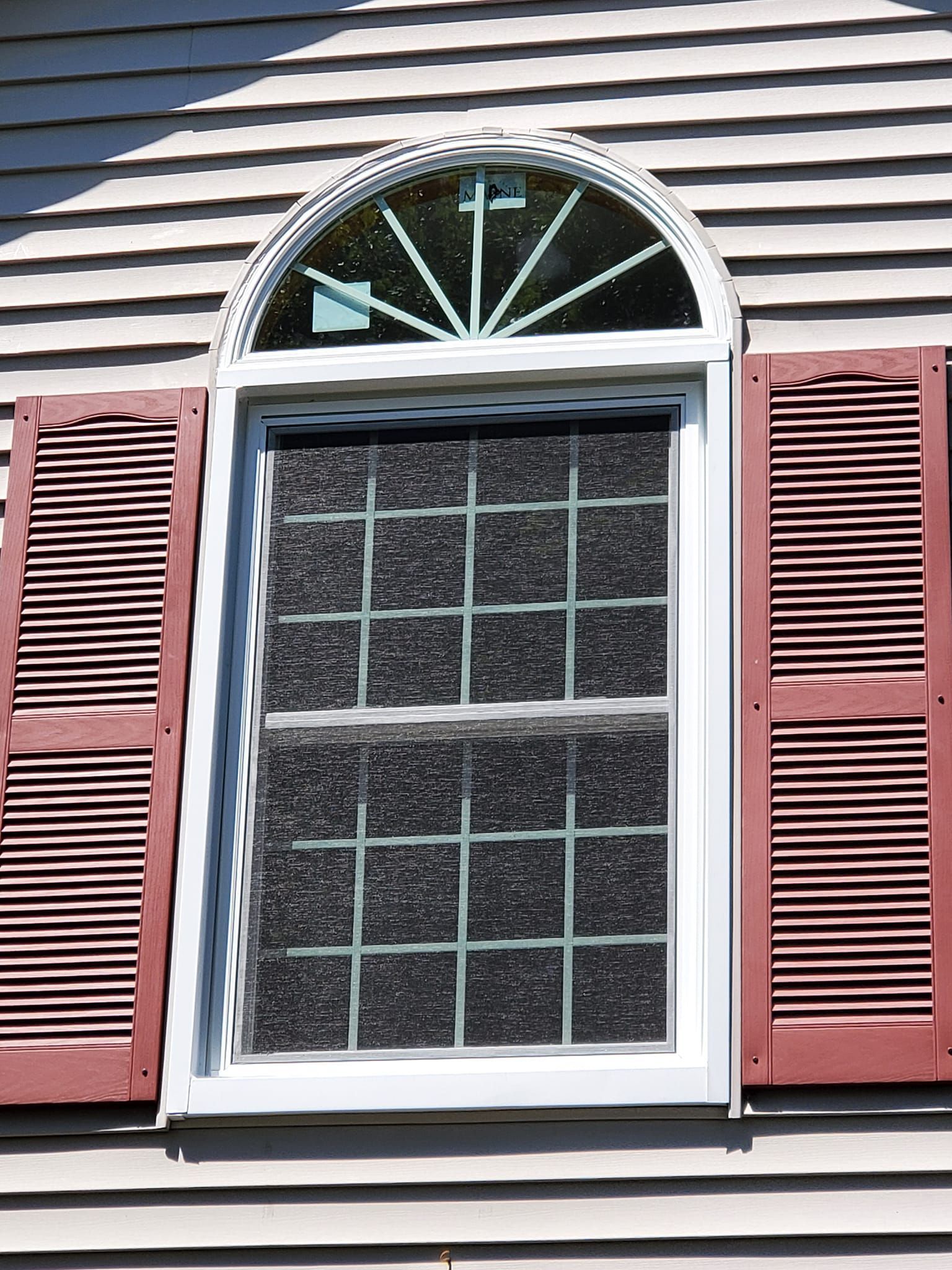 White-framed window with red shutters on a house exterior, topped by an arched fanlight.