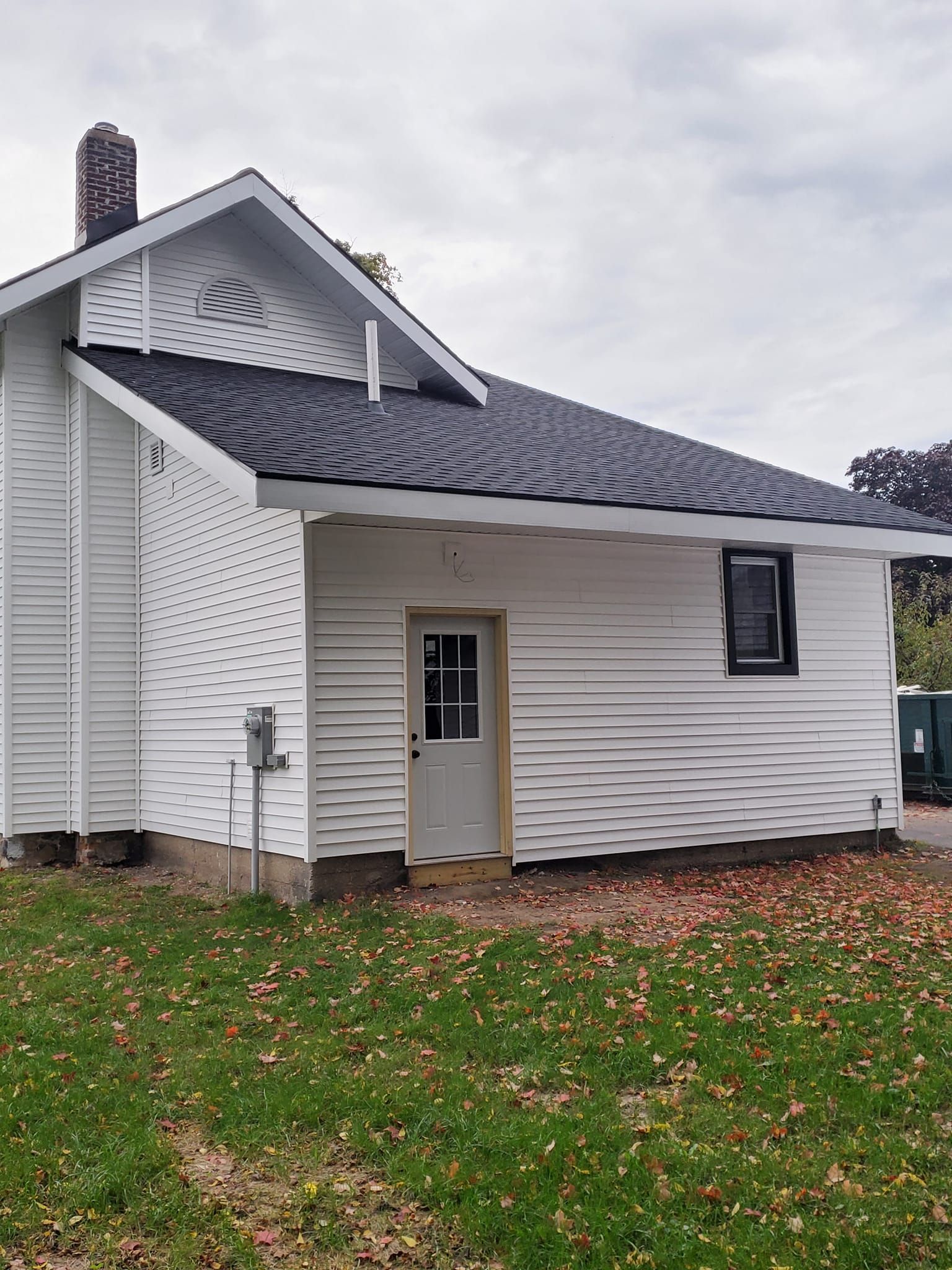 White house exterior with gray roof, small side entrance, and autumn leaves on the lawn