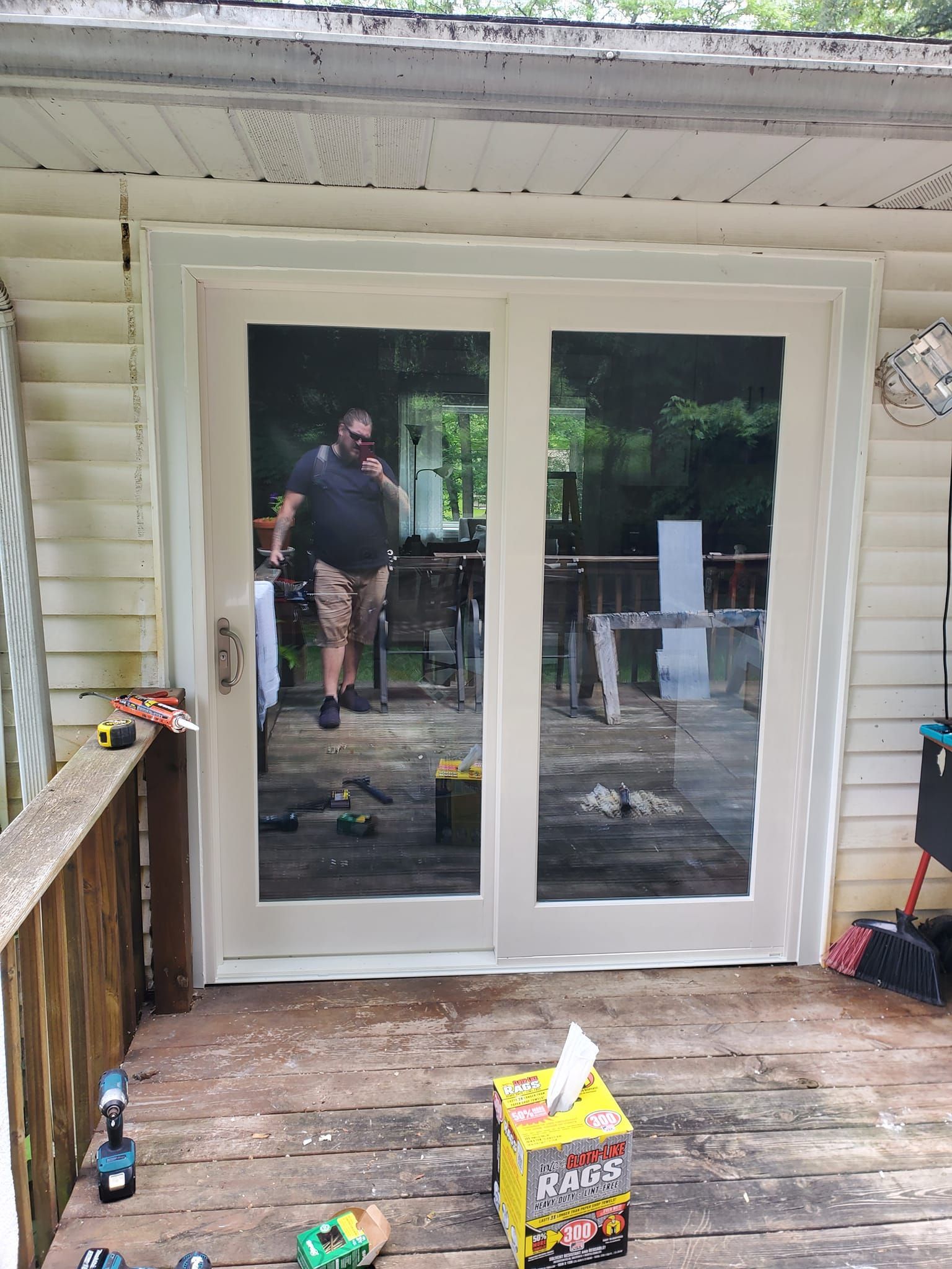 White sliding glass doors on a porch, with a man reflected standing outside.