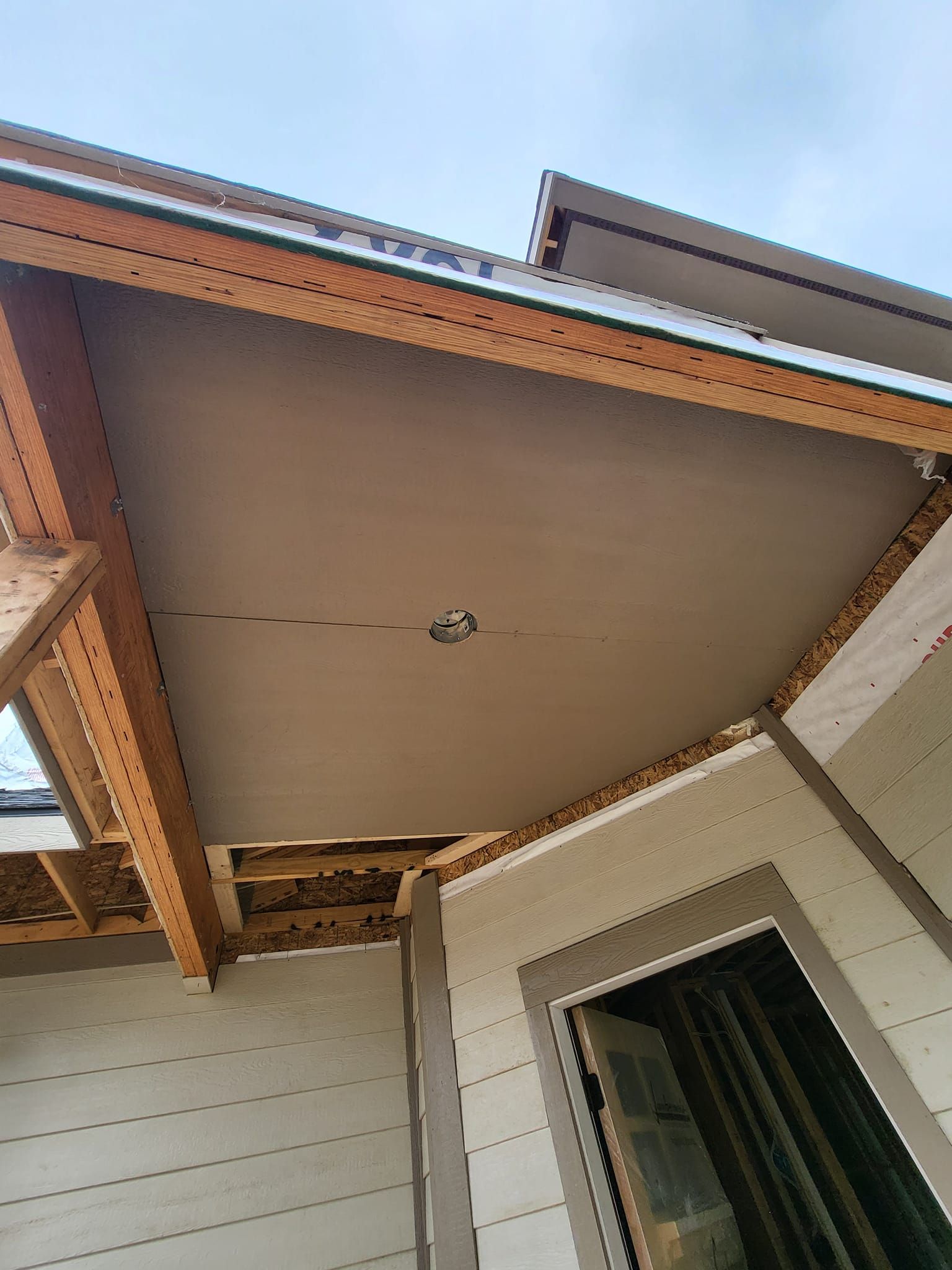 Upward view of a house porch ceiling with exposed beams, siding, and a window below