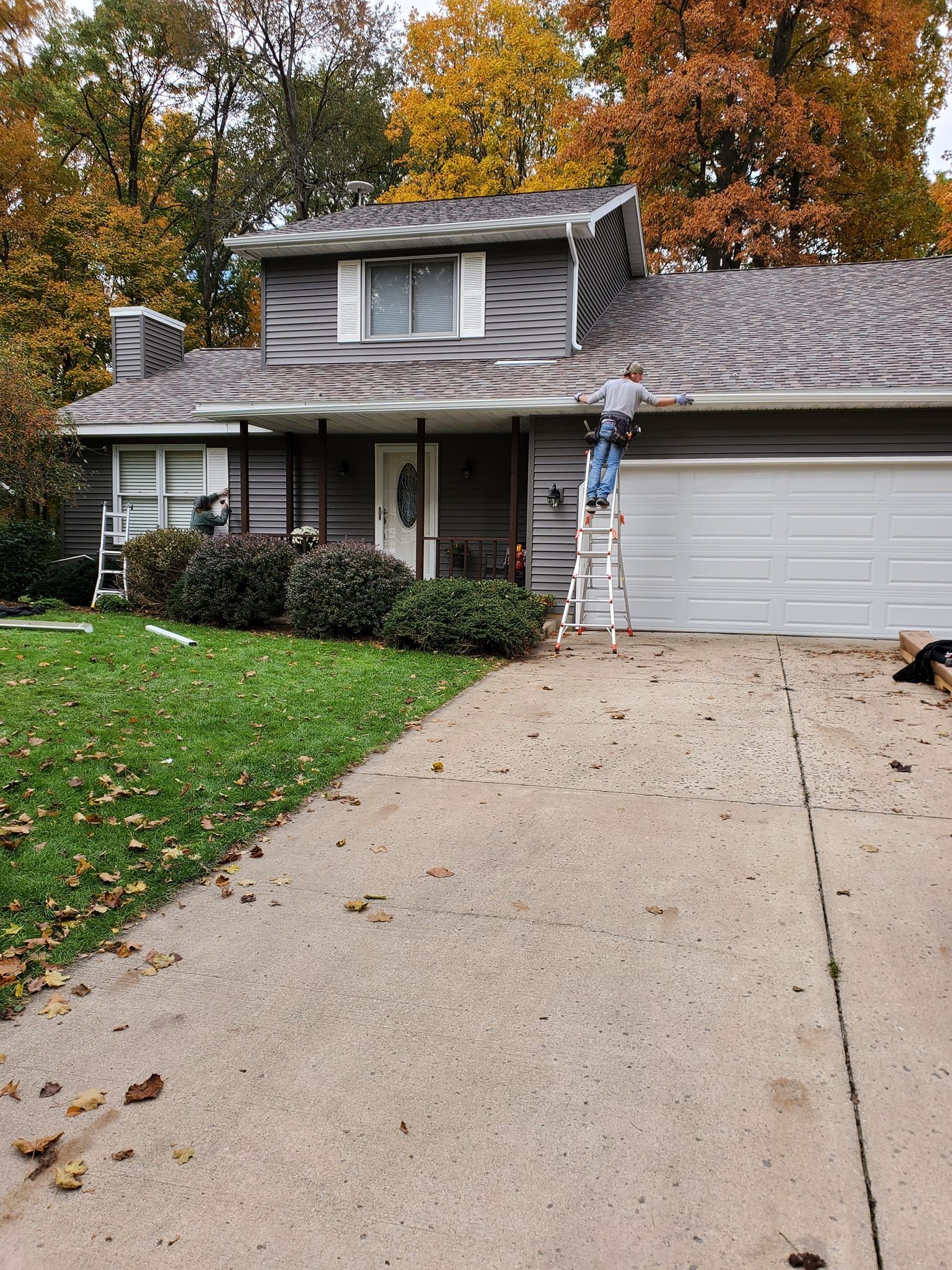 Suburban two-story house with a driveway, garage, and autumn trees in front yard