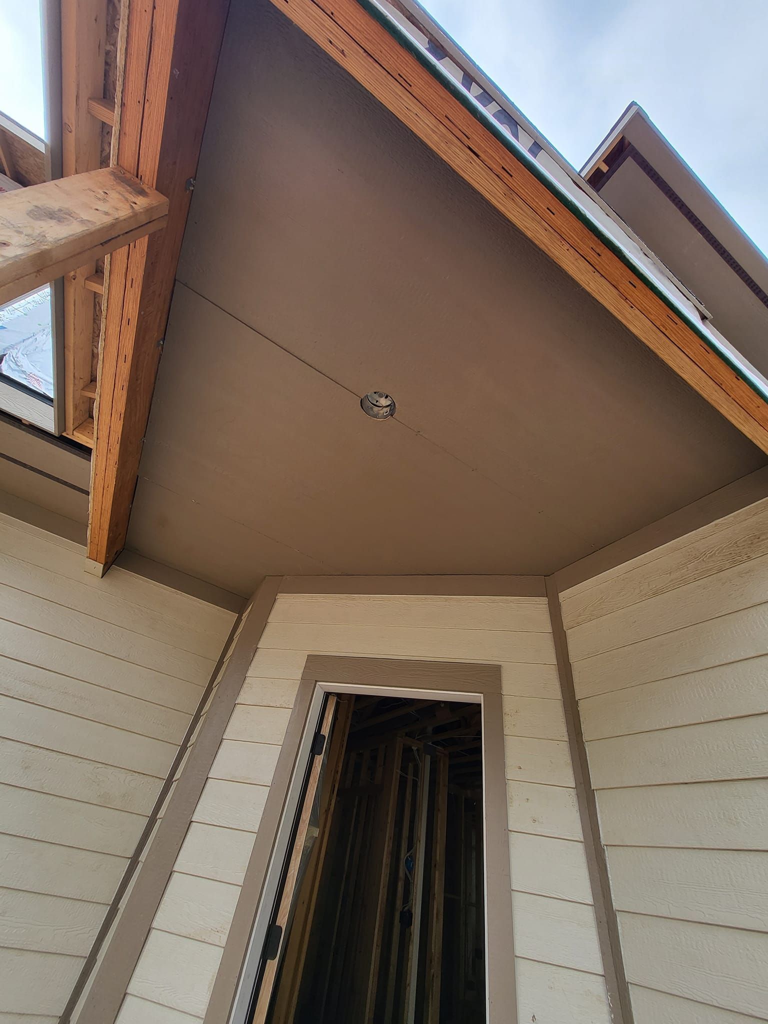 Upward view of a home porch ceiling with exposed wooden beams and an open doorway below
