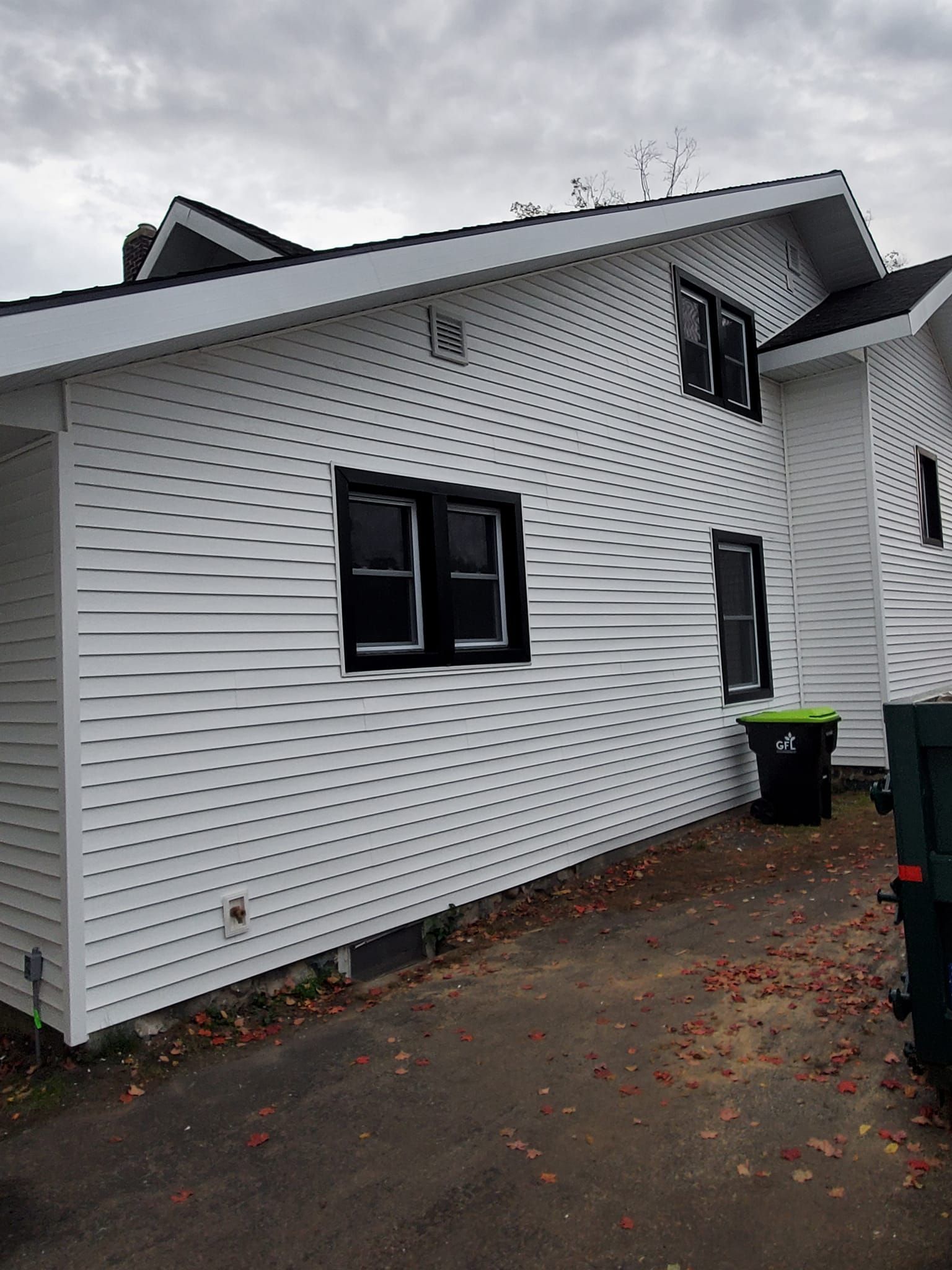 White house exterior with black shutters and a wet driveway on a cloudy day