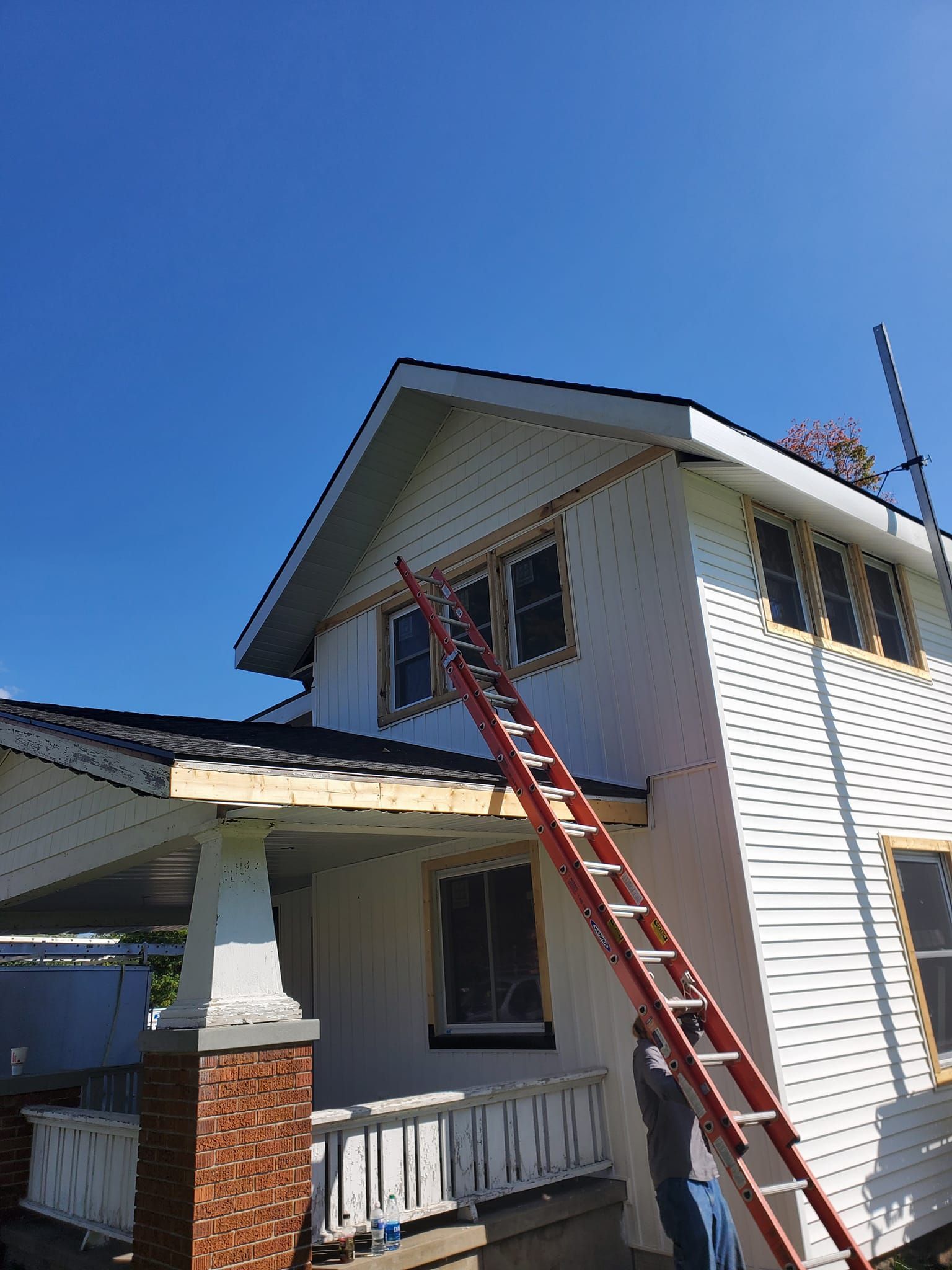 Two-story house with a red ladder leaning to the roof under a clear blue sky