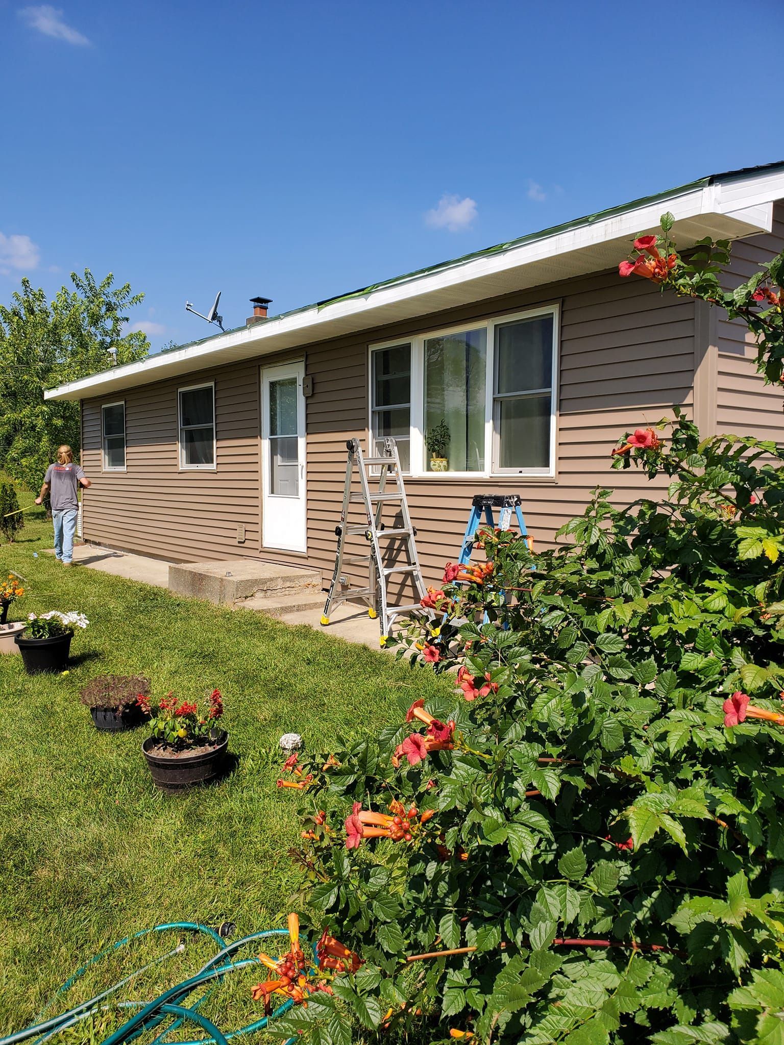 Single-story beige house with white trim, flower beds, and a bright blue sky