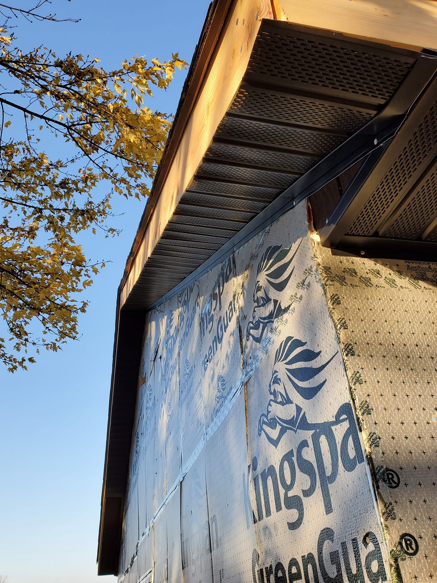 Wall-mounted mural on a building under a clear blue sky, with trees and autumn leaves nearby