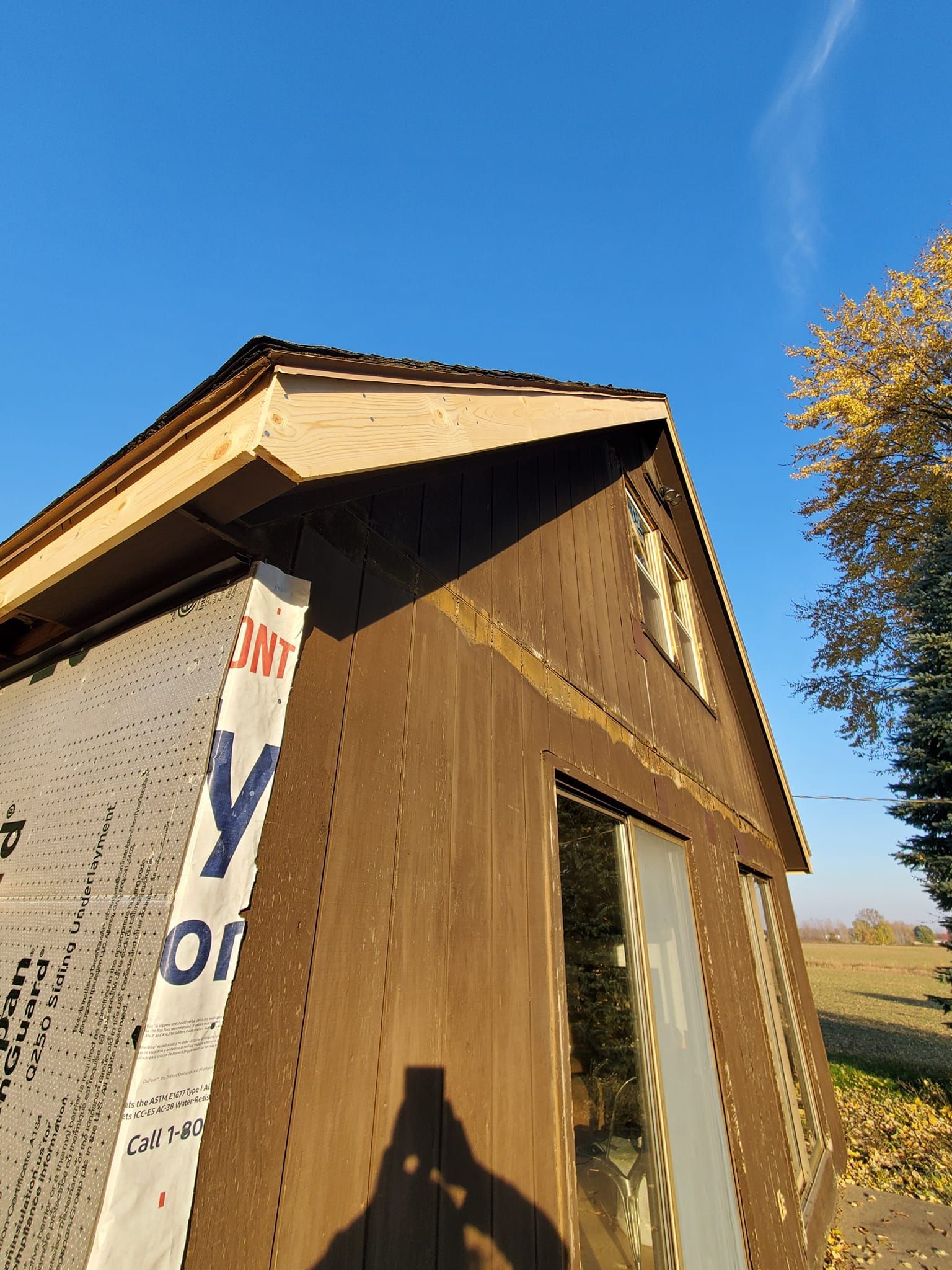 Small wooden shed with unfinished siding and a slanted roof under a clear blue sky.