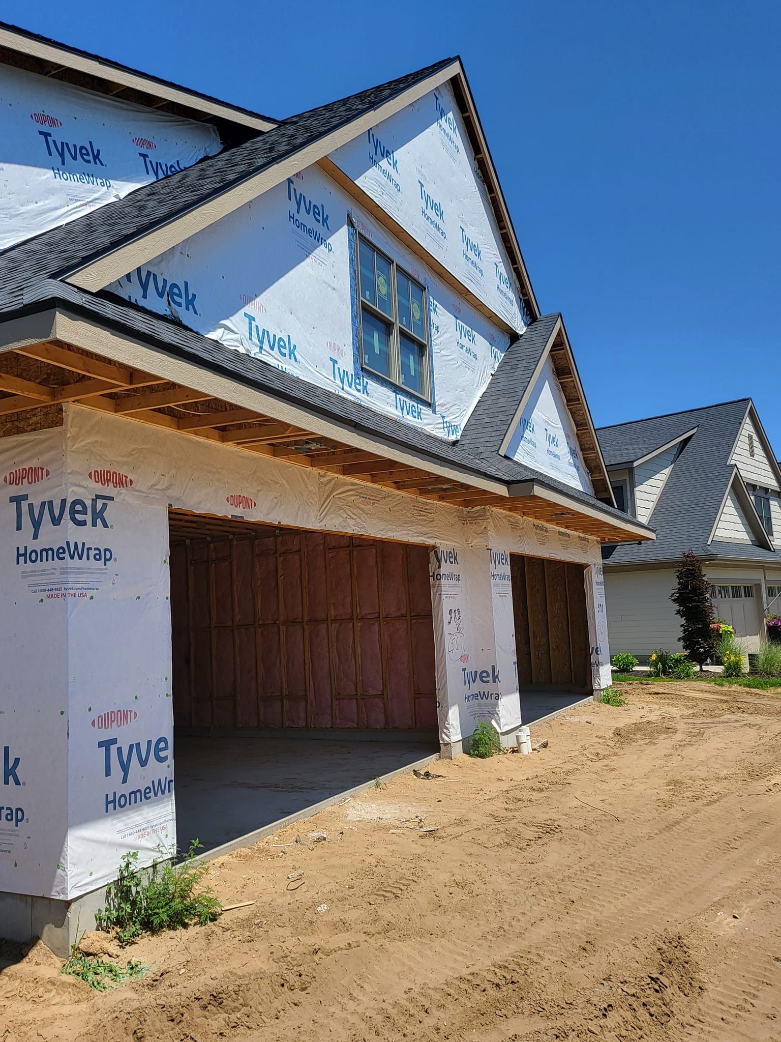 New houses under construction with Tyvek wrap and open garage on a dirt lot
