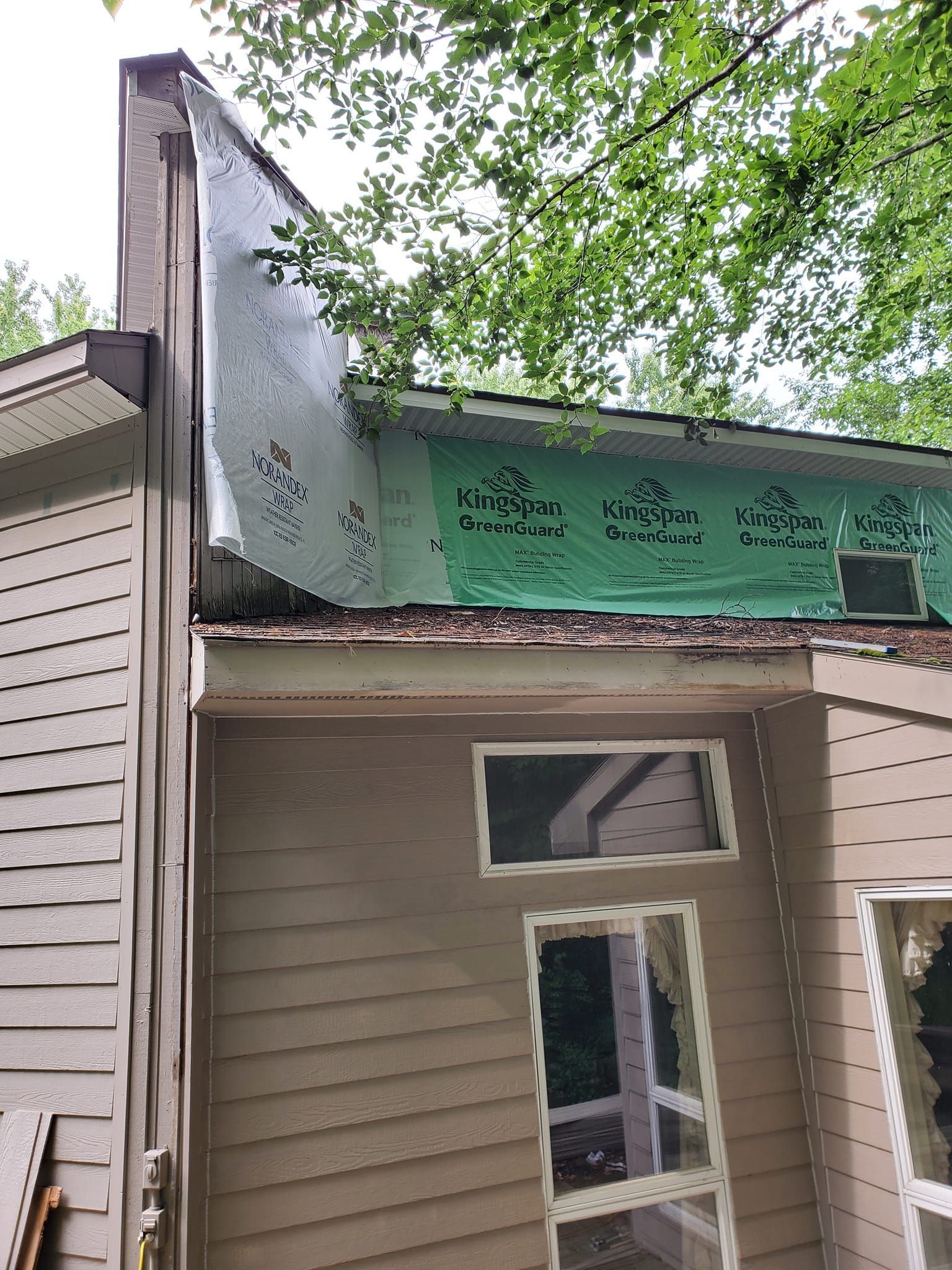 Damaged storefront roof with peeling green signboard and white siding under trees