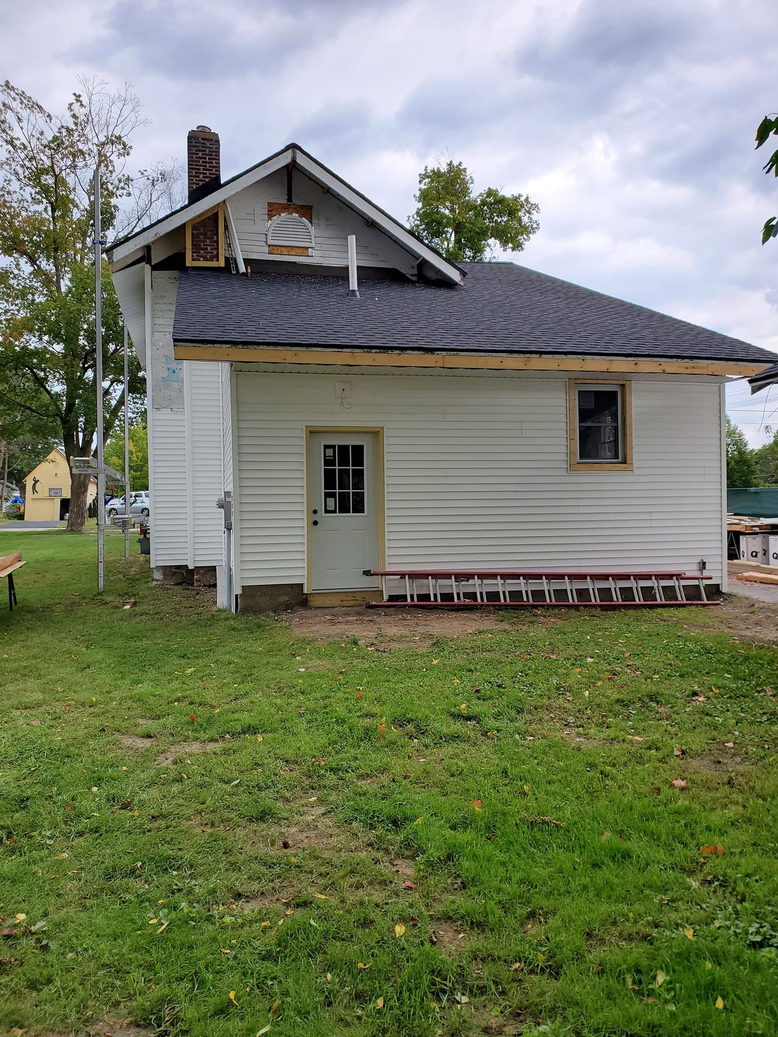 Small white house with a gray roof and porch, viewed from the side on a grassy lot.
