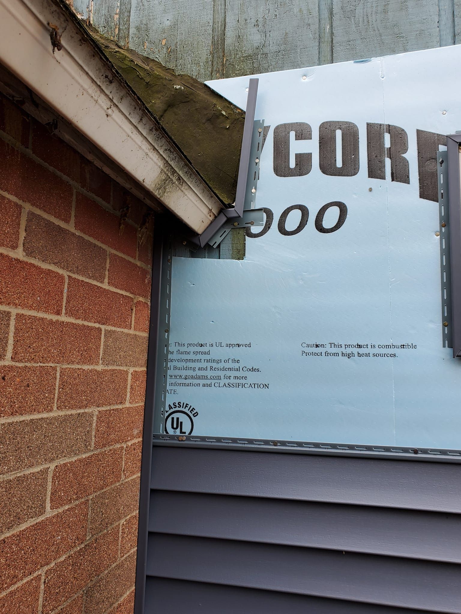 Storefront window under roof eaves, with partial white signage and brick wall beside it.