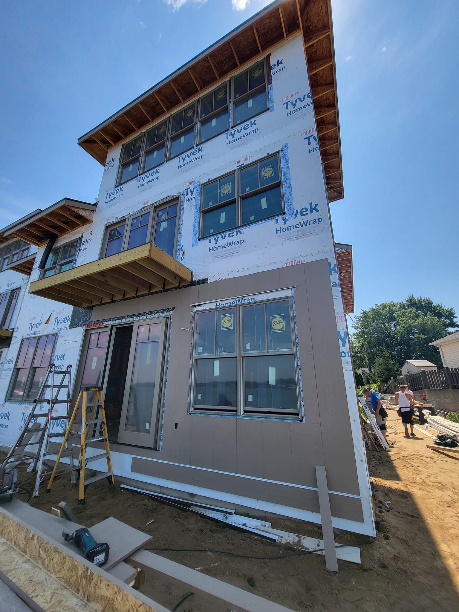 Three-story house under construction with white exterior and scaffolding under a blue sky