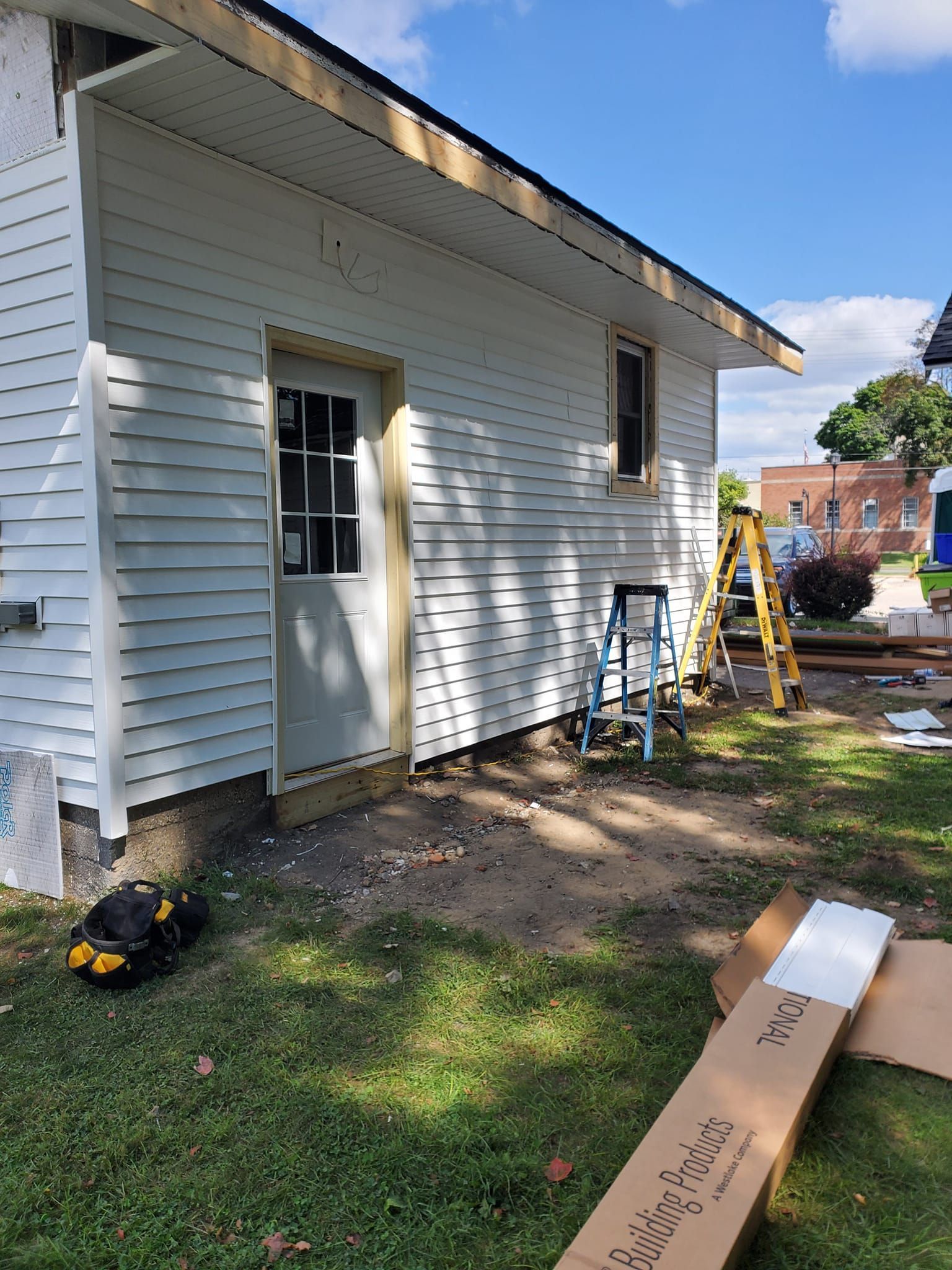 White house exterior with a worker’s ladder, tools, and construction materials on the ground