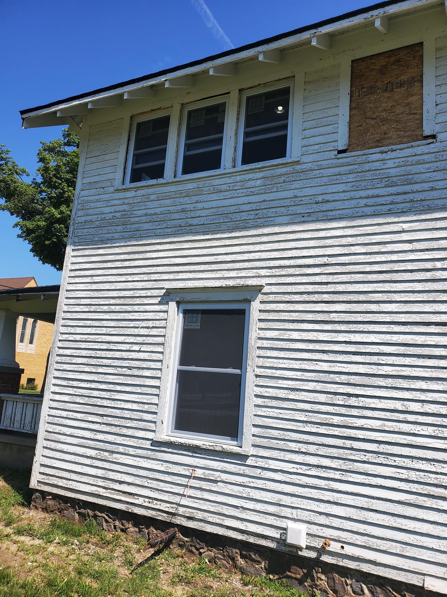 Two-story white house with boarded upper windows and a single lower window under a blue sky