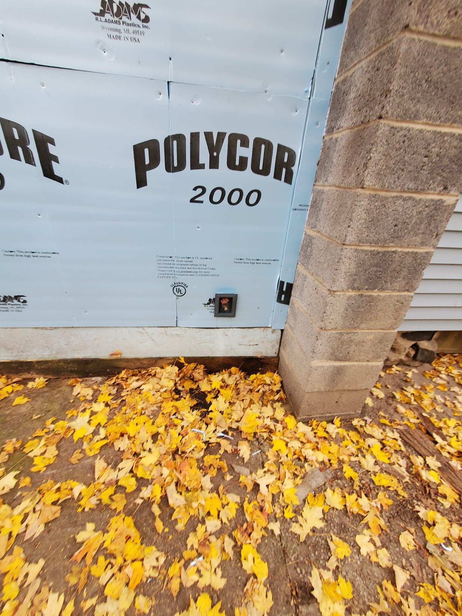 POLYCORE 2000 wrap on a wall beside a cinder block pillar, with yellow leaves scattered below