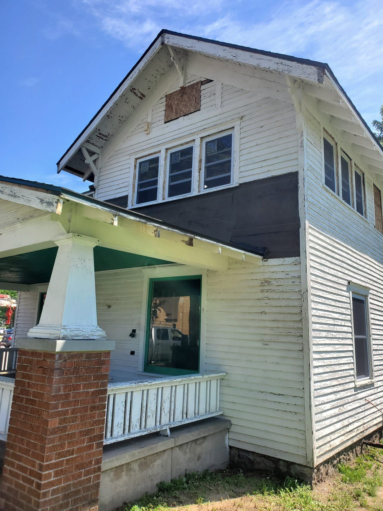 Two-story white house with brick porch columns and a green-roofed front porch under a blue sky