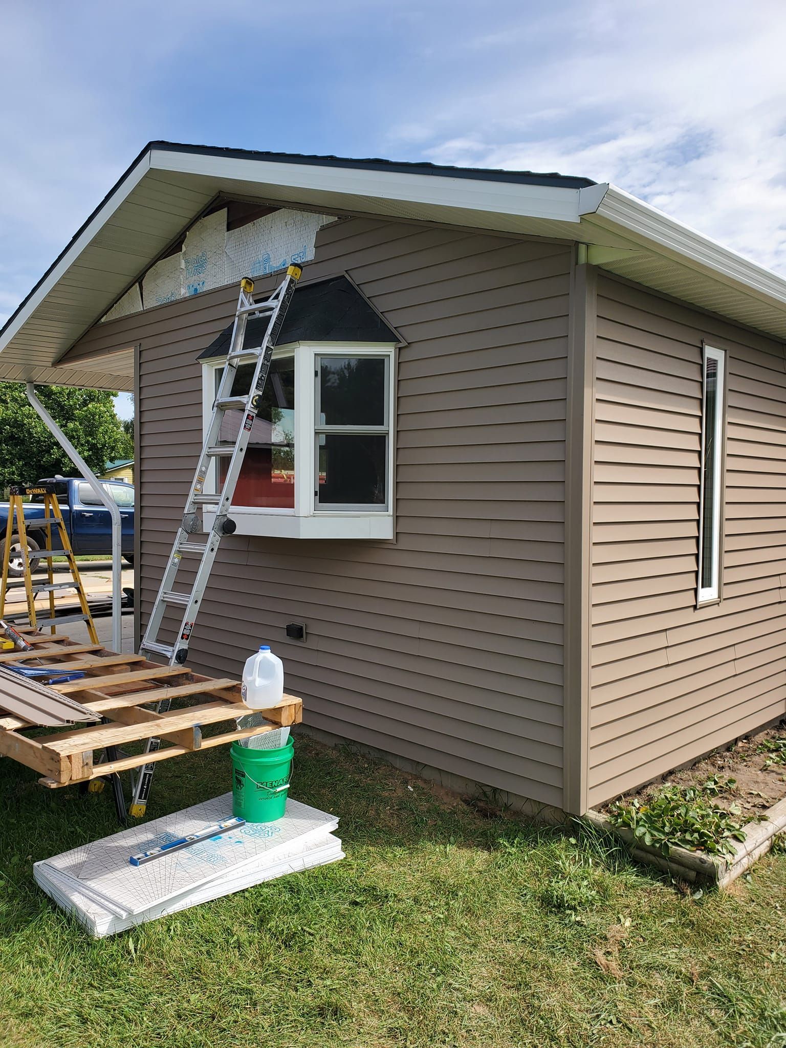 Worker painting tan house exterior from ladder near window