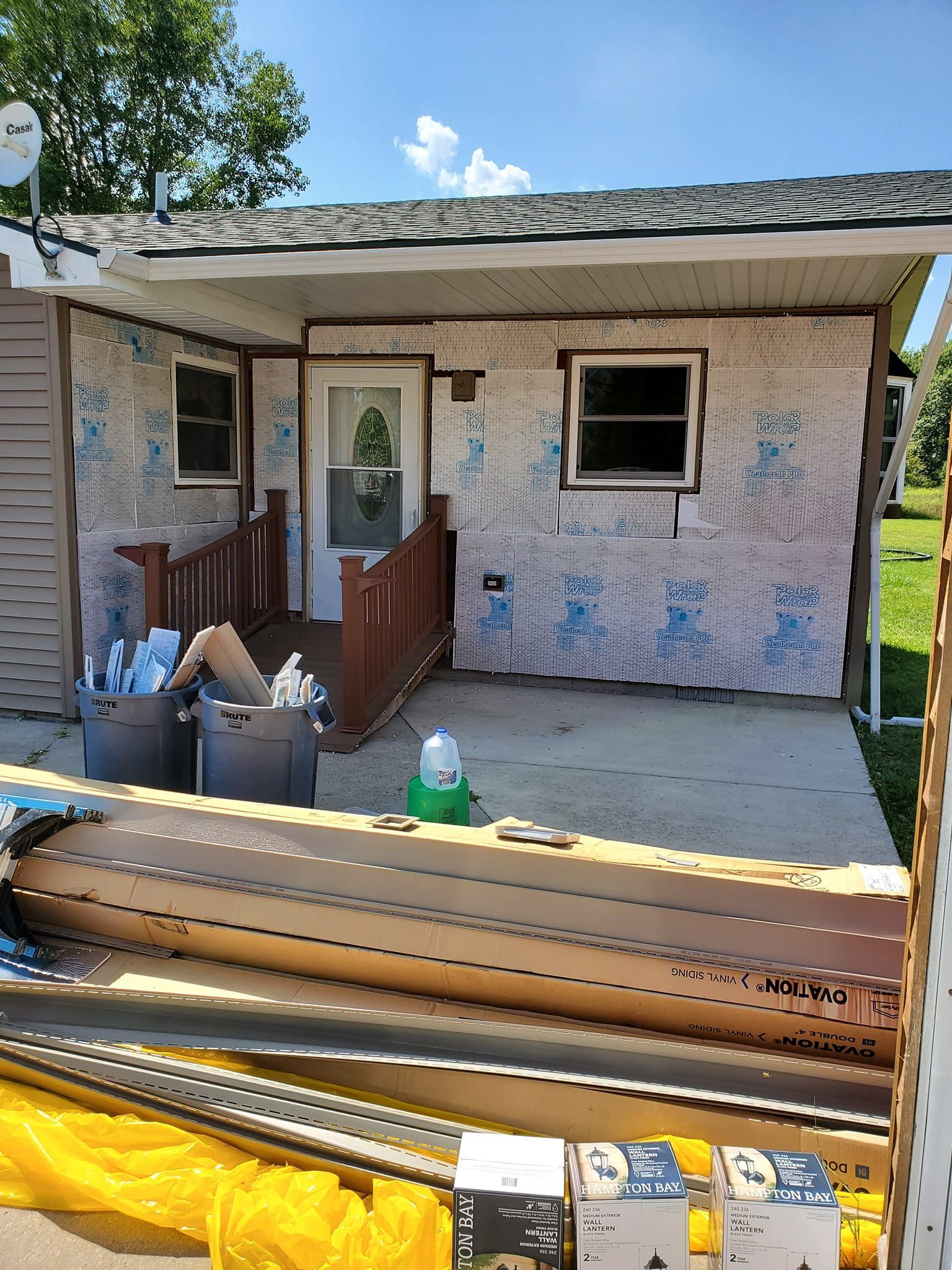 Front of a small house with a porch, window, and construction materials stacked in the foreground.