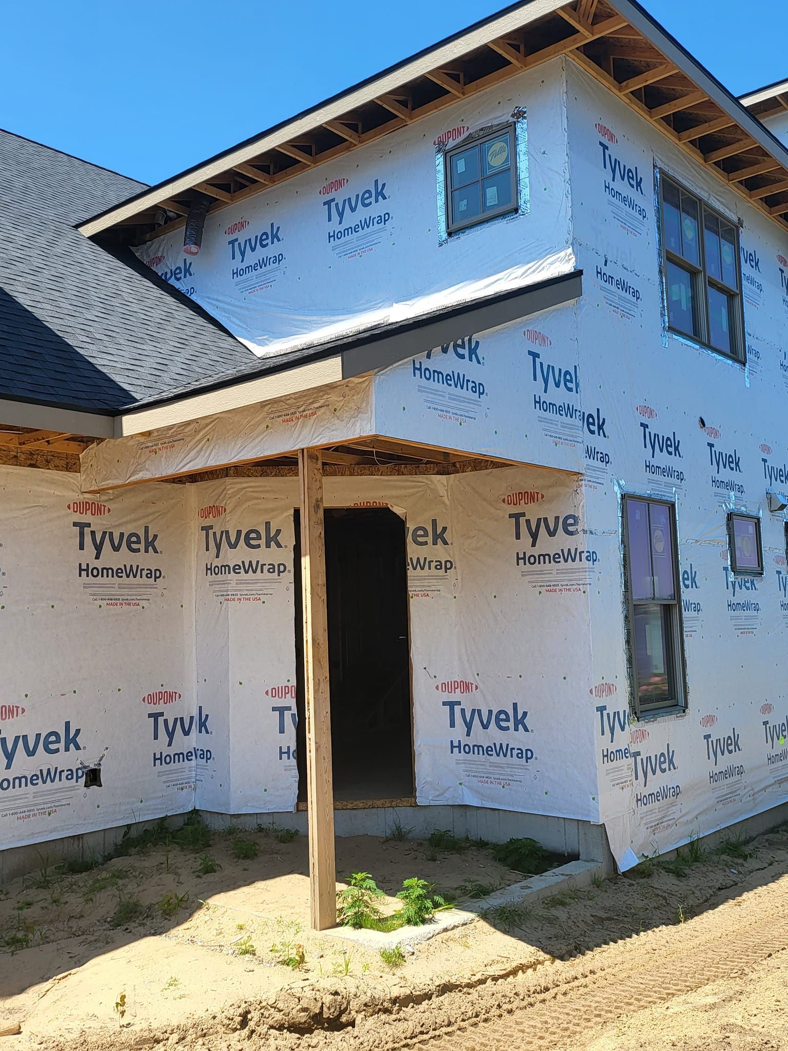 Two-story house under construction, wrapped in Tyvek house wrap with unfinished porch and windows.