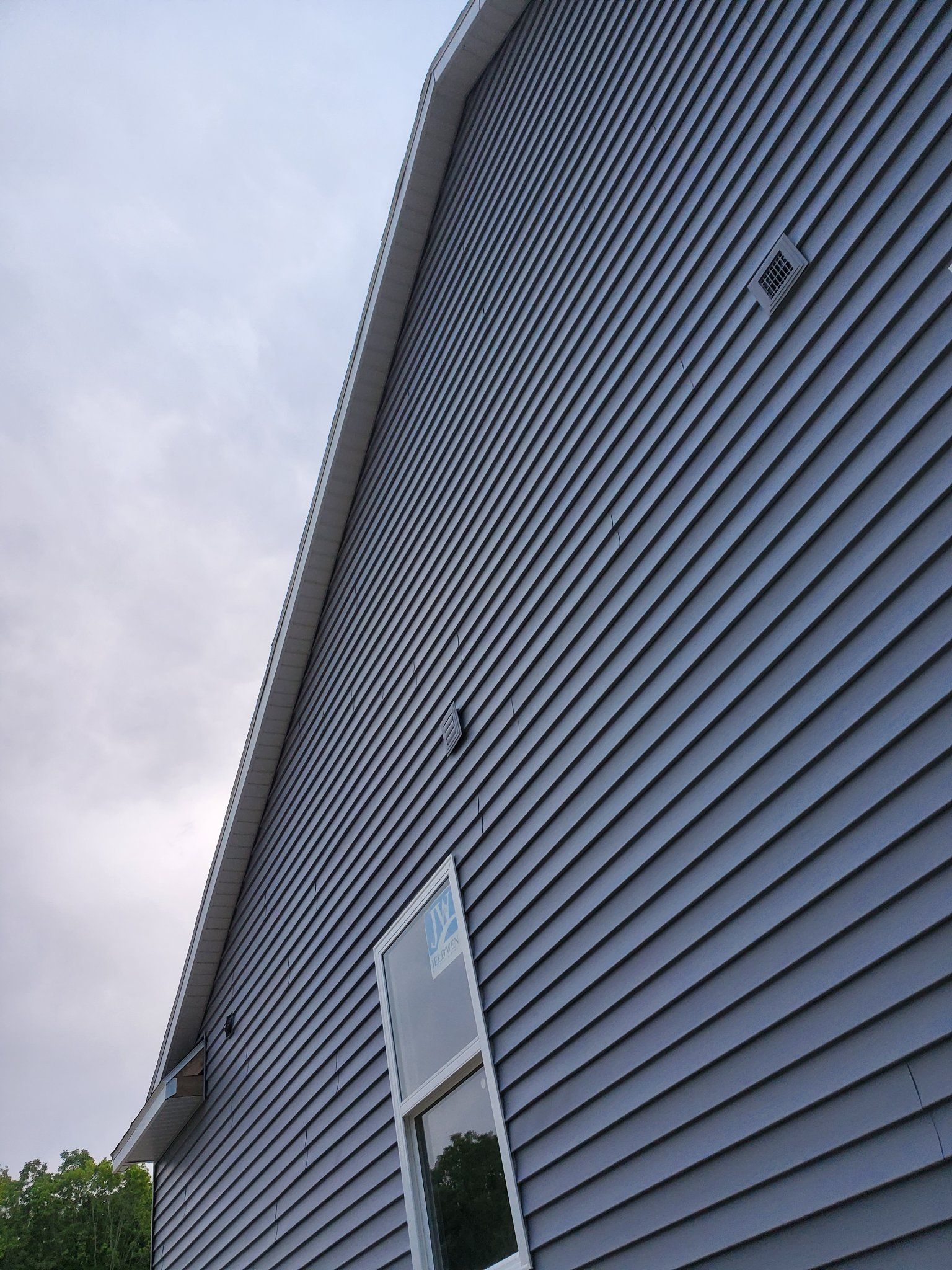 Close-up of a gray-sided house exterior with a window and cloudy sky above