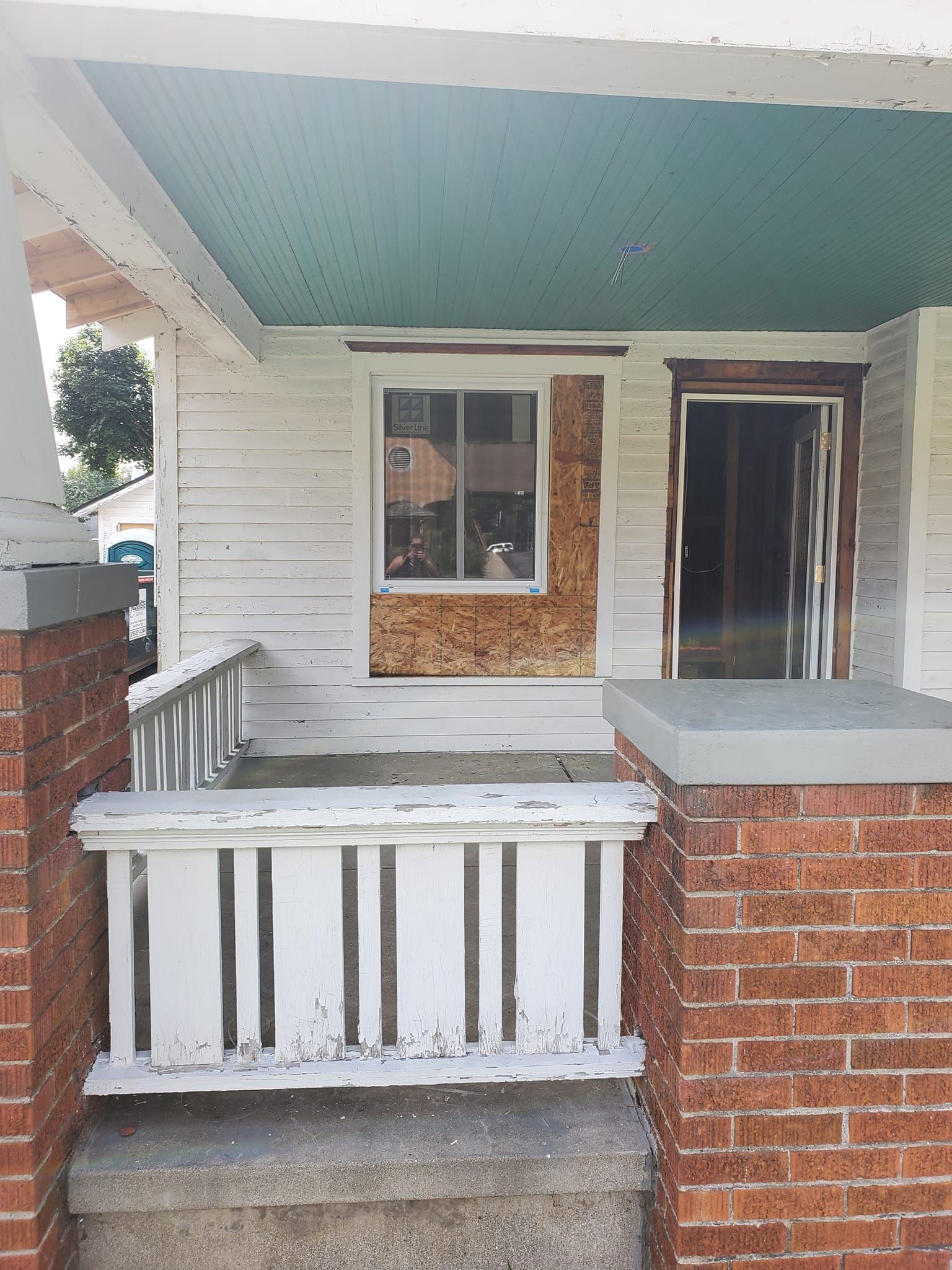 Front porch with white siding, teal ceiling, brick half-wall, and an open doorway.