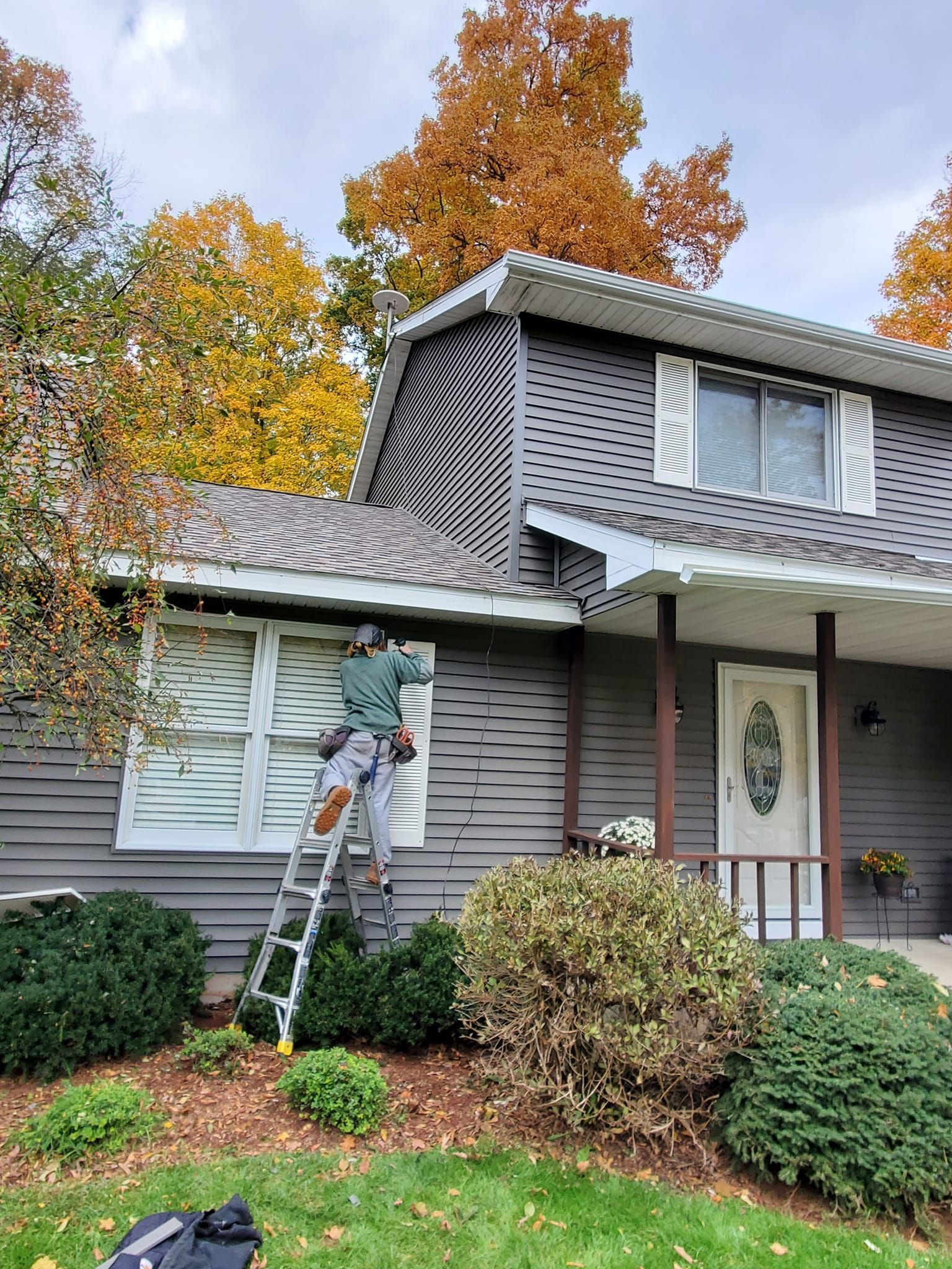 Worker on ladder painting a house exterior with autumn trees in the background
