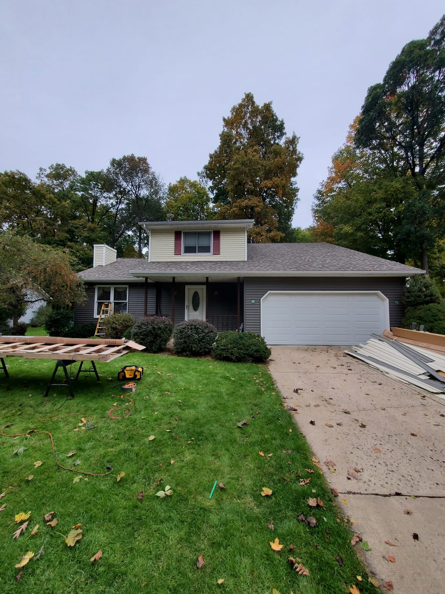 Suburban house with a two-car garage, front lawn, and picnic table under overcast skies