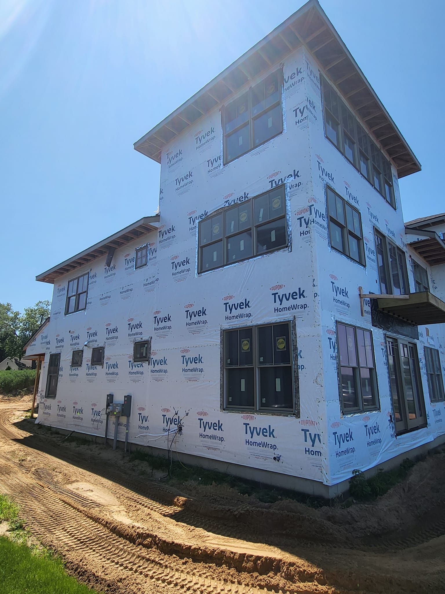 Partially built two-story white house with scaffolding-like markings beside a dirt road under a blue sky