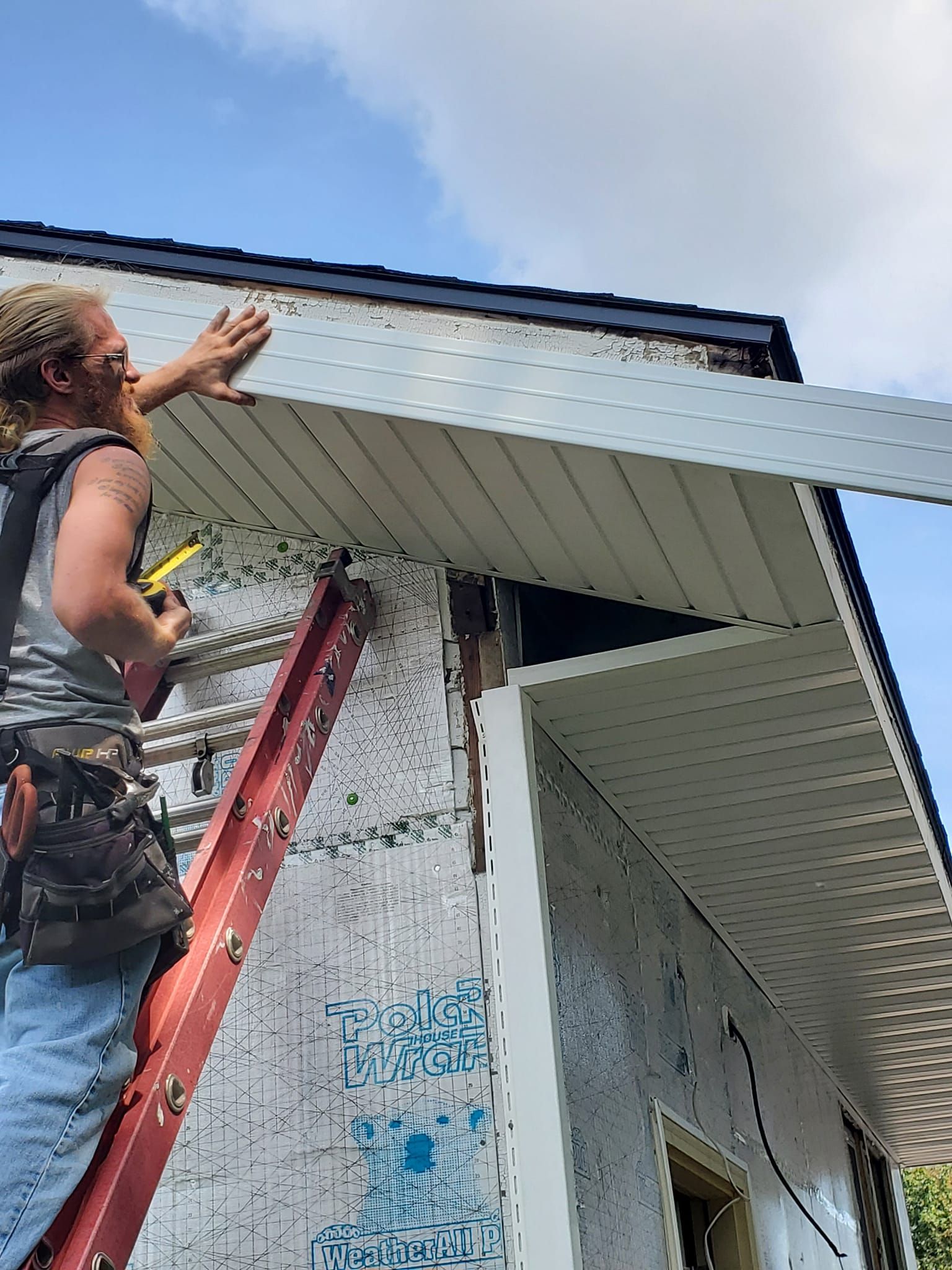 Person on a ladder working on the roof edge of a house exterior