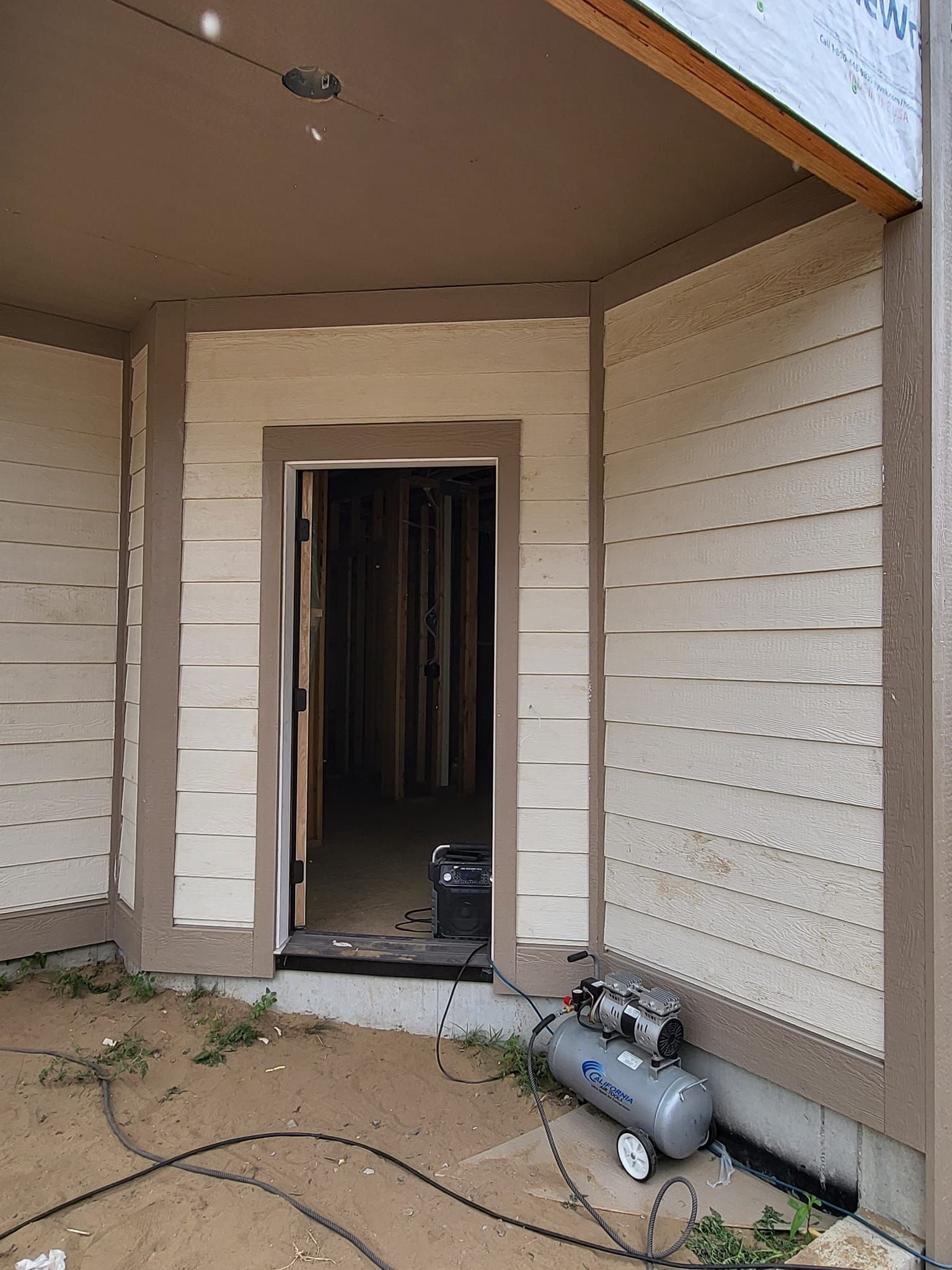 Damaged house entryway with broken trim, exposed interior, and a compressor on the porch