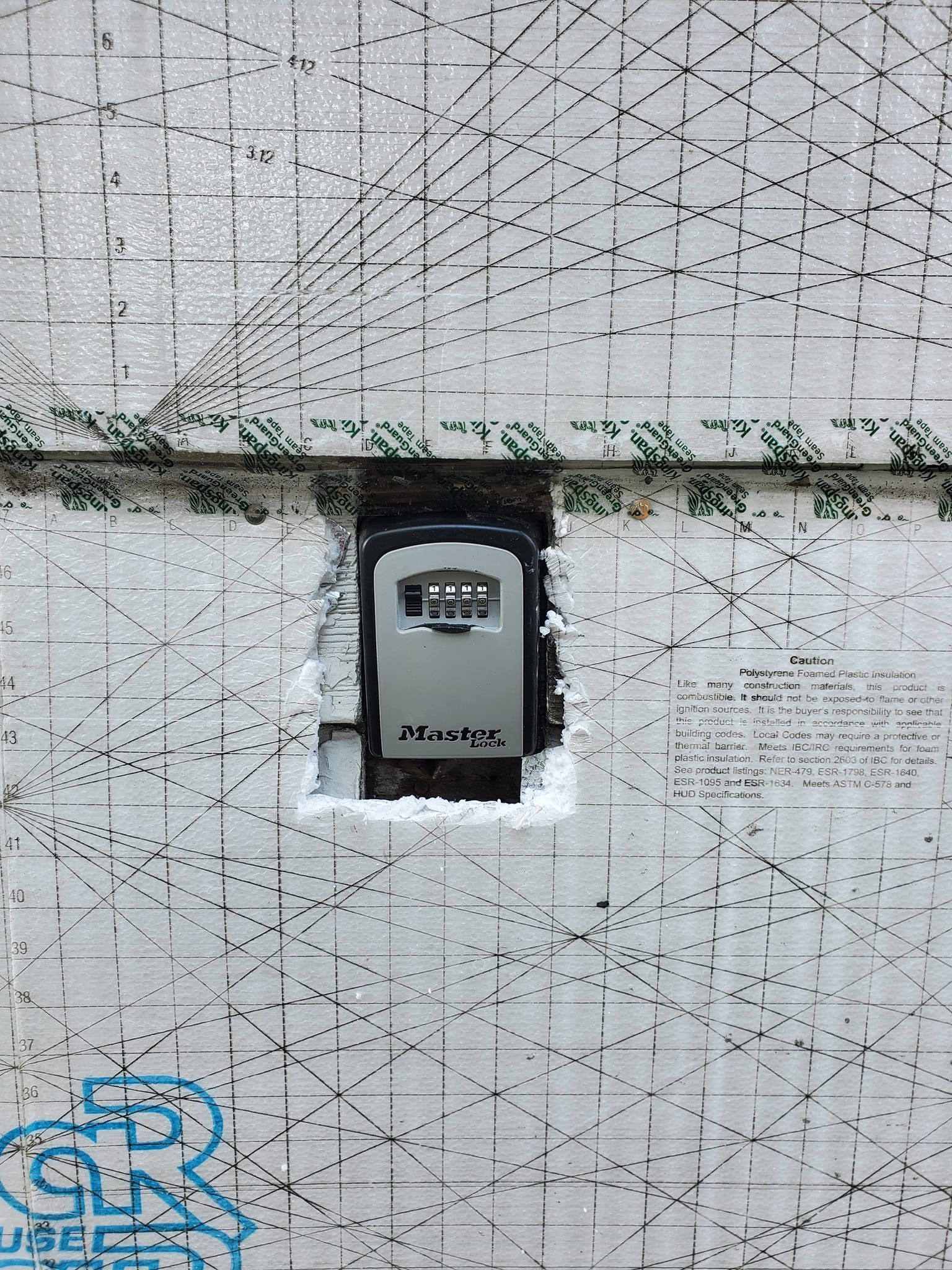Wall-mounted weathered utility meter on a white cracked wall with graffiti and a green strip above it