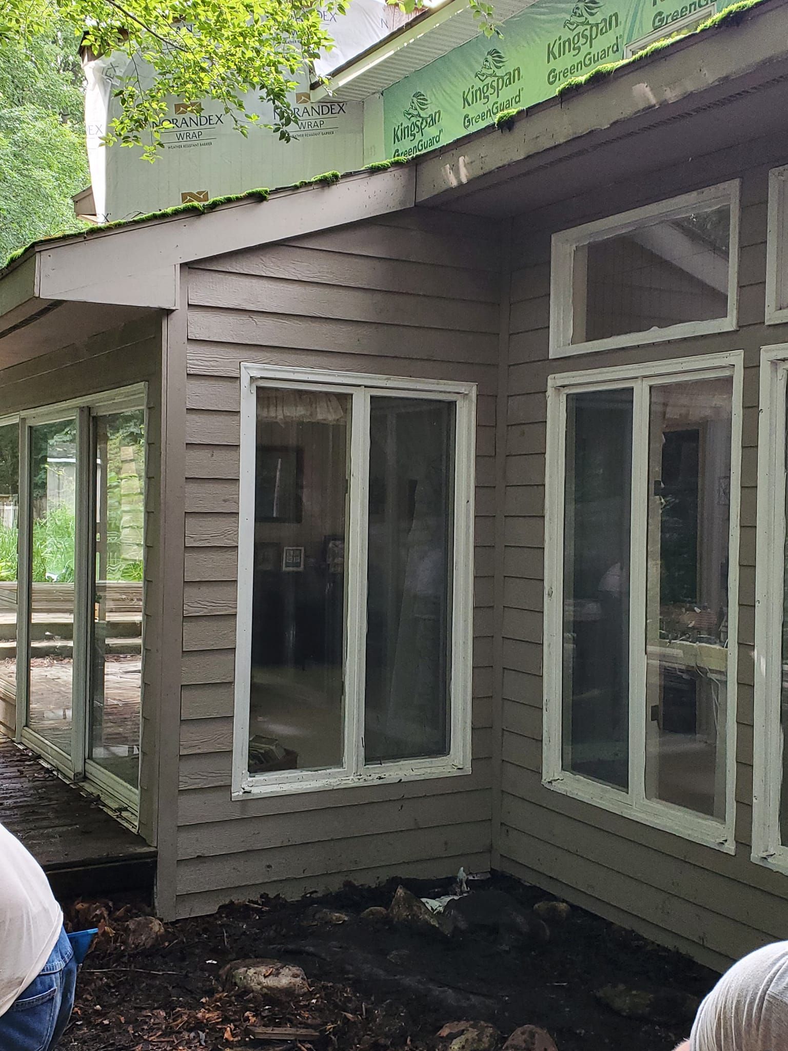 House exterior with damaged siding and broken windows near a porch under green awning