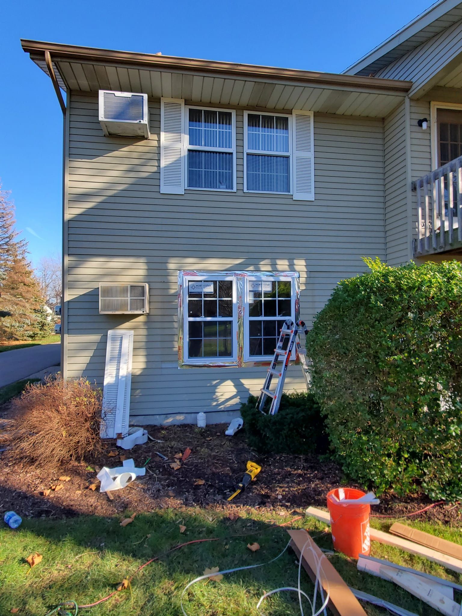 Apartment exterior with beige siding, windows, bushes, and a small ladder by the front