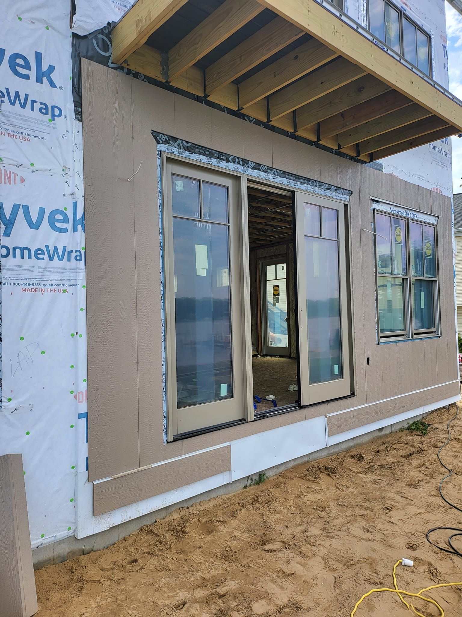 Partially finished house exterior with a sliding glass door and windows under a raised deck