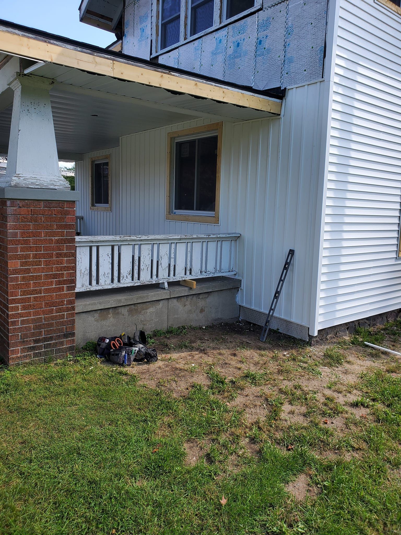 Small house porch with white siding, brick pillar, window, and lawn in front.