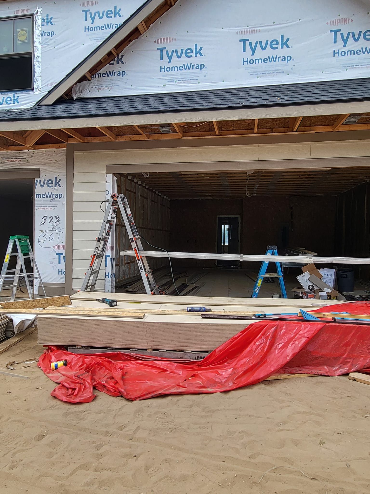 Partially built house with open garage, ladders, and construction materials on a dirt lot