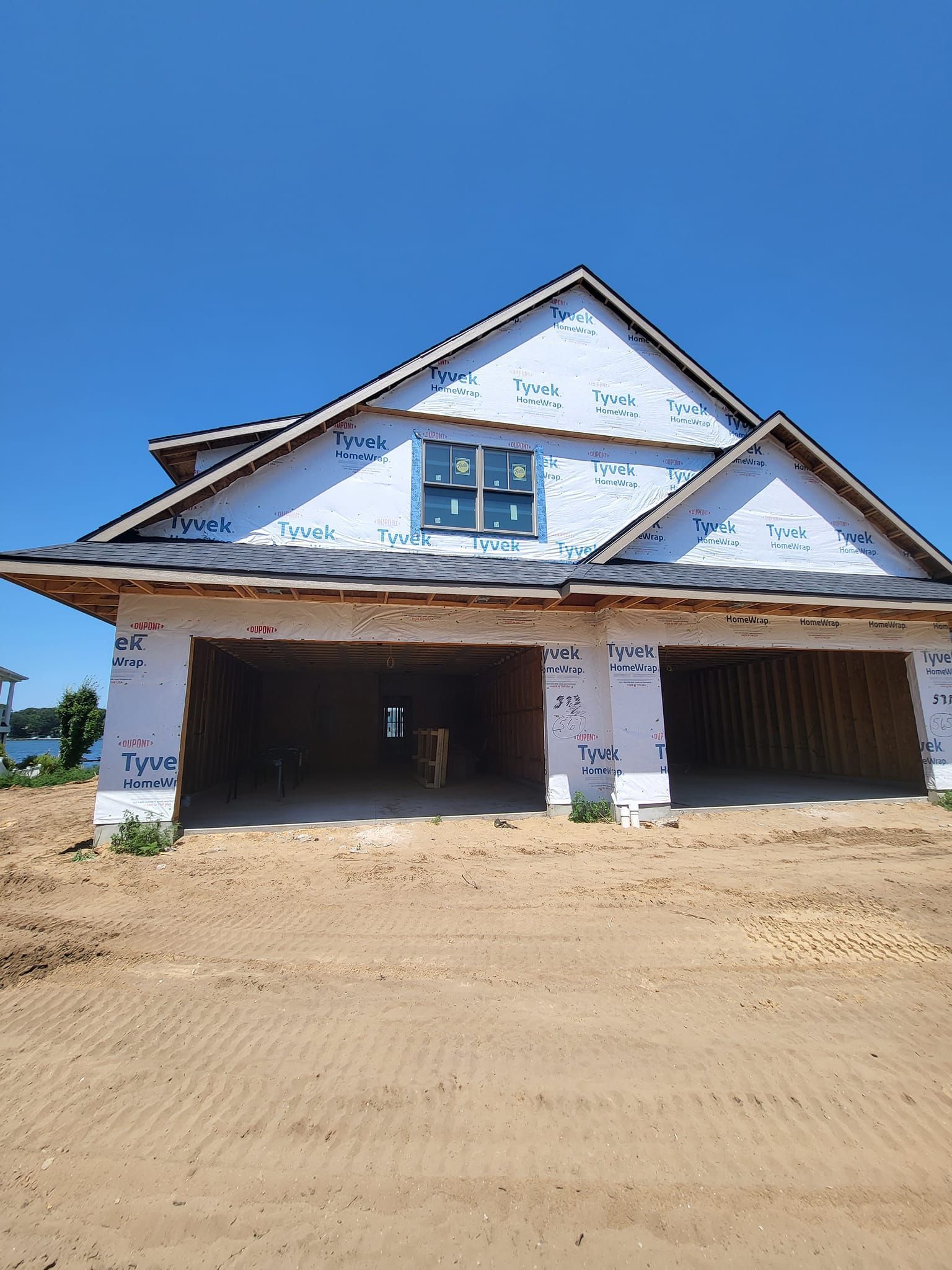 Partially built house with white siding, exposed framing, and two open garage bays under a blue sky