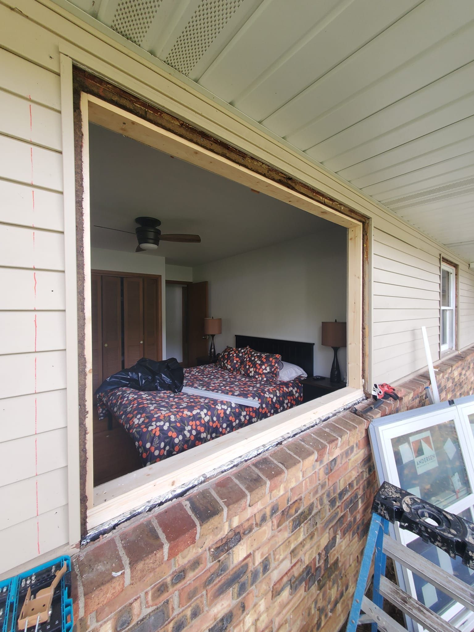 Open window view into a bedroom with a bed covered in a dark floral comforter and a ceiling fan.