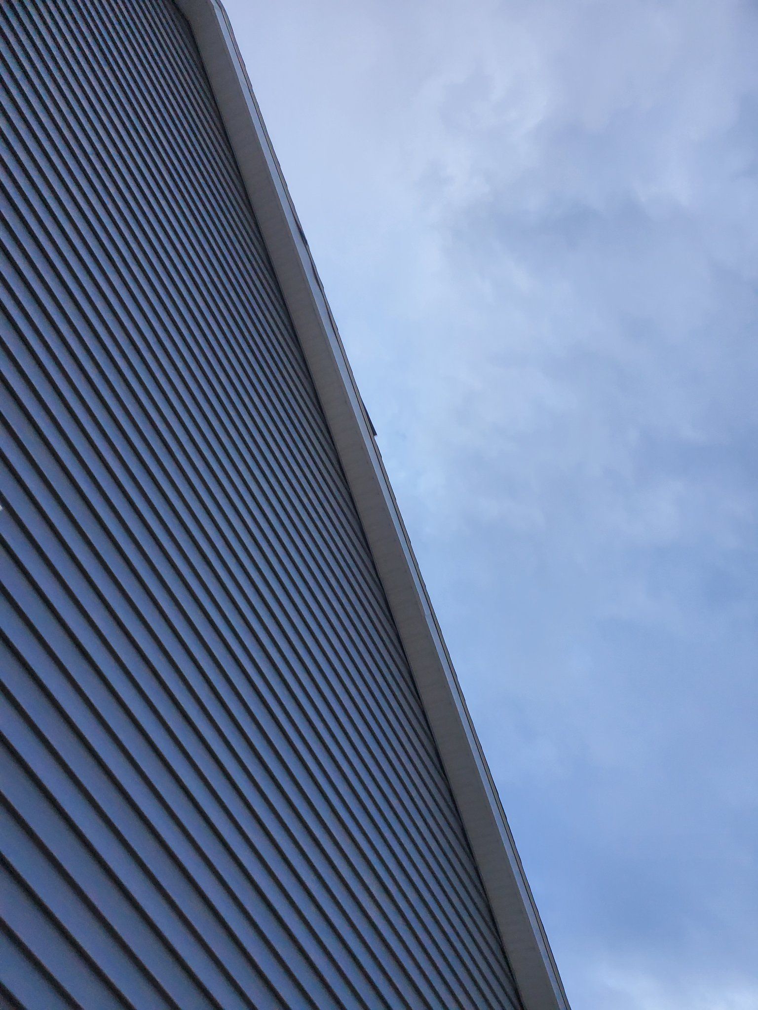 Angled view of a building facade with blue-gray siding against a cloudy sky