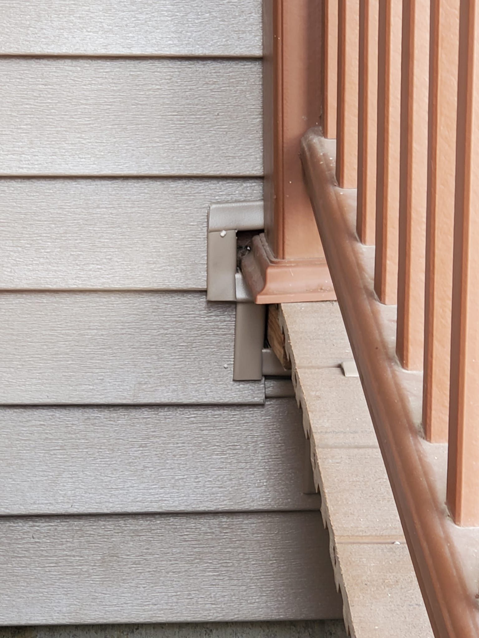 Close-up of a staircase railing mounted to a gray-sided exterior wall with metal brackets.