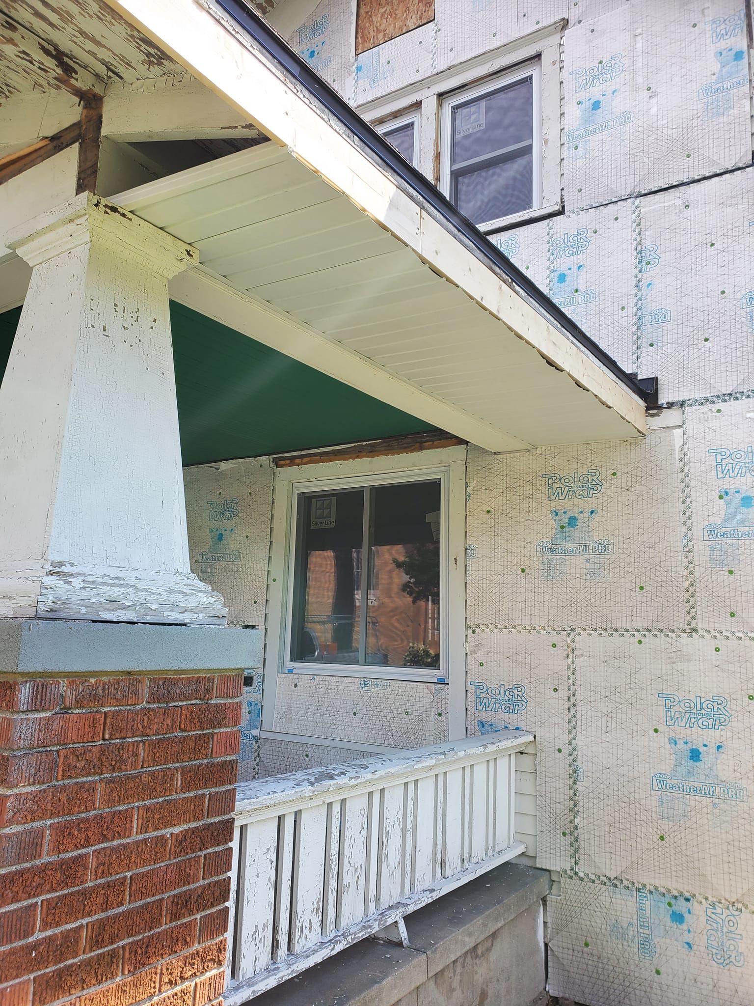 Old apartment porch with peeling white paint, red brick column, and a small window under an overhang