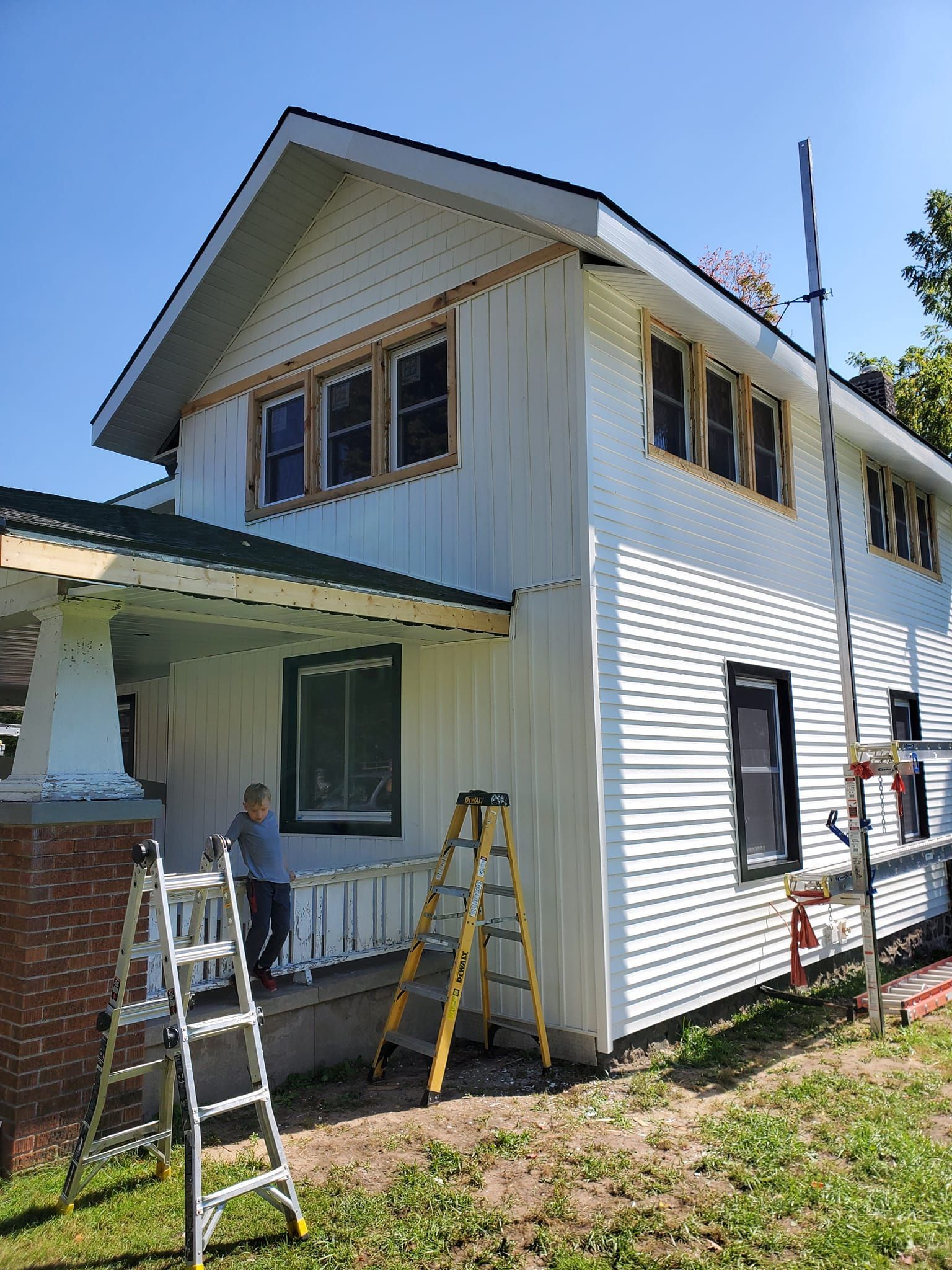 White two-story house with ladders and scaffolding, suggesting exterior repairs or painting