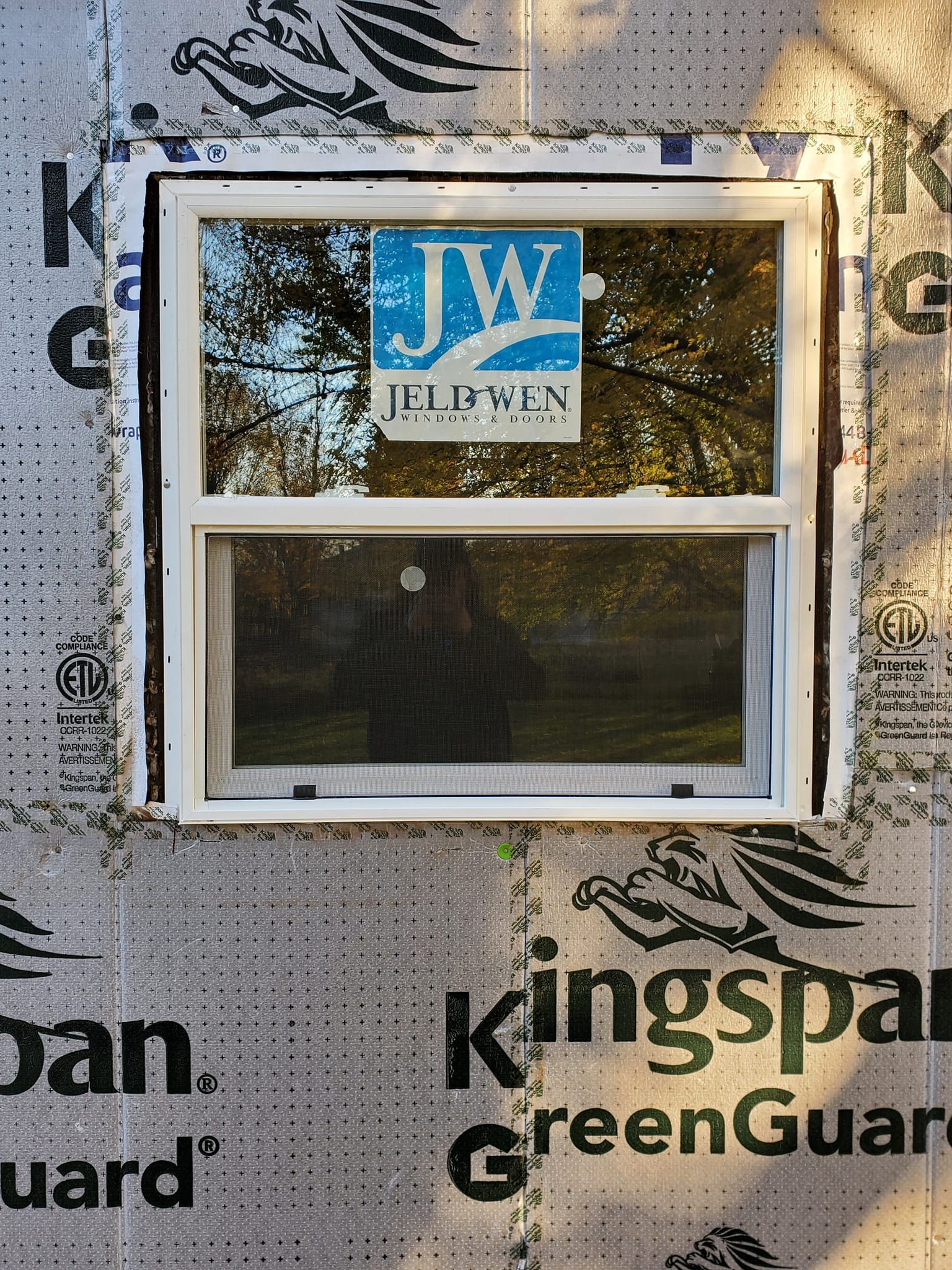 Small white-framed window in a wall of Kingspan GreenGuard sheathing with a JW label above it.