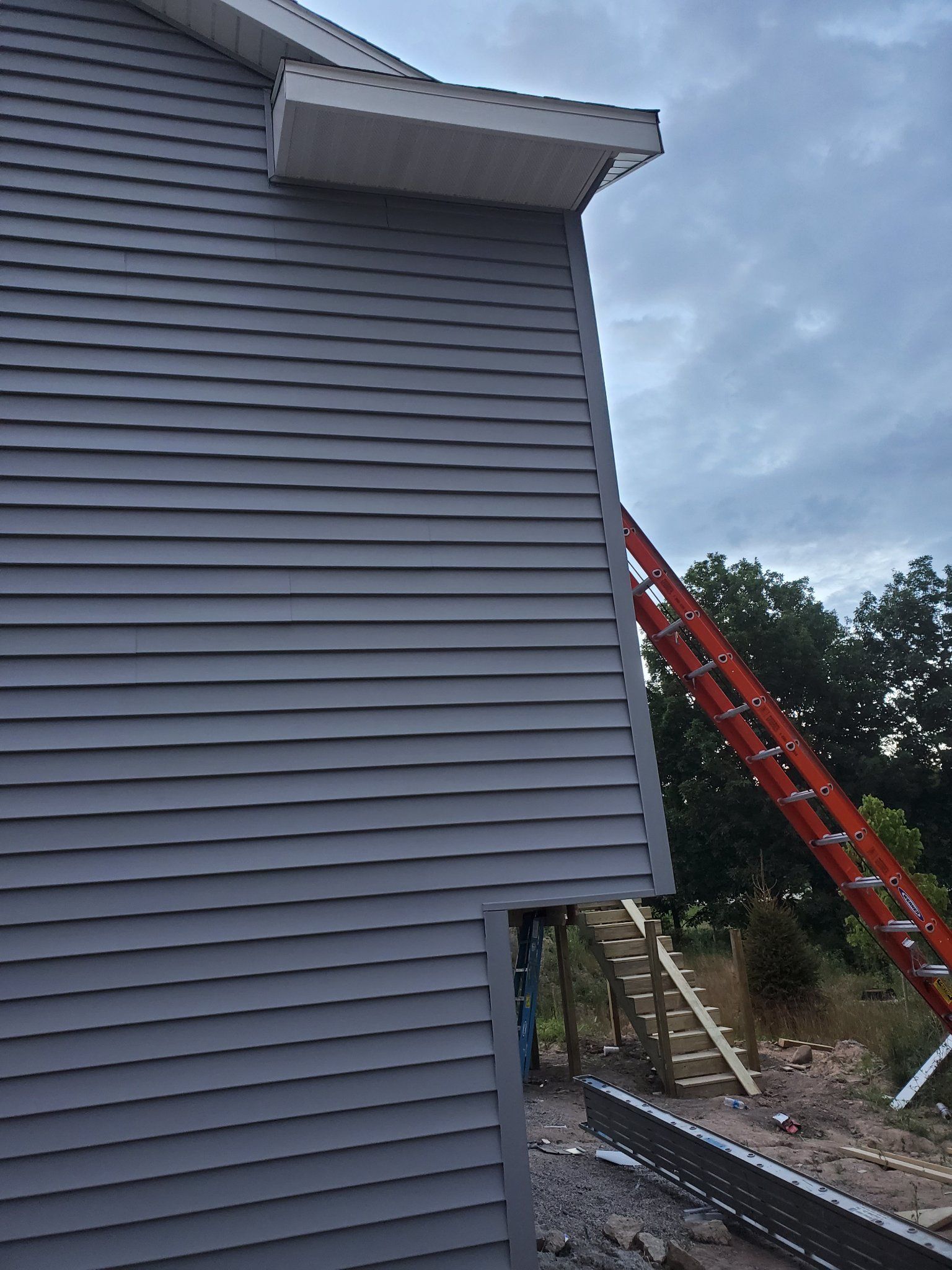 Side of a gray house with red ladders leaning against it under a cloudy sky.