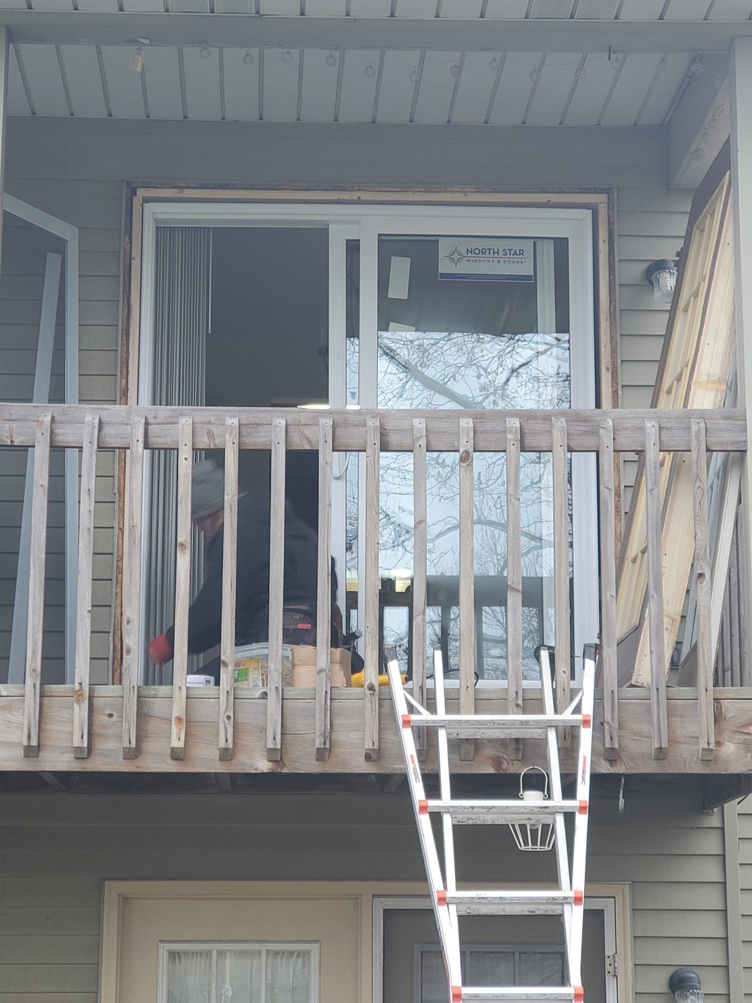 Apartment balcony with damaged wooden railing and a ladder leaning up to it.