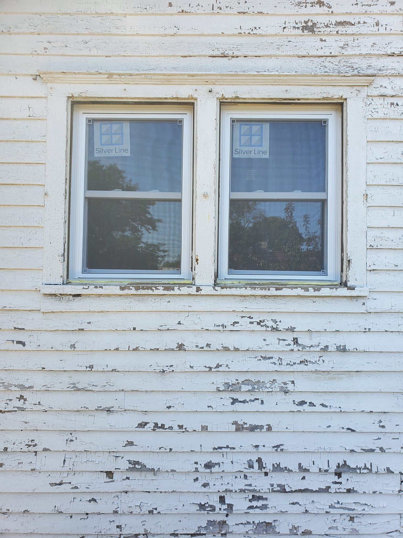 Two small windows on a weathered white wooden house exterior