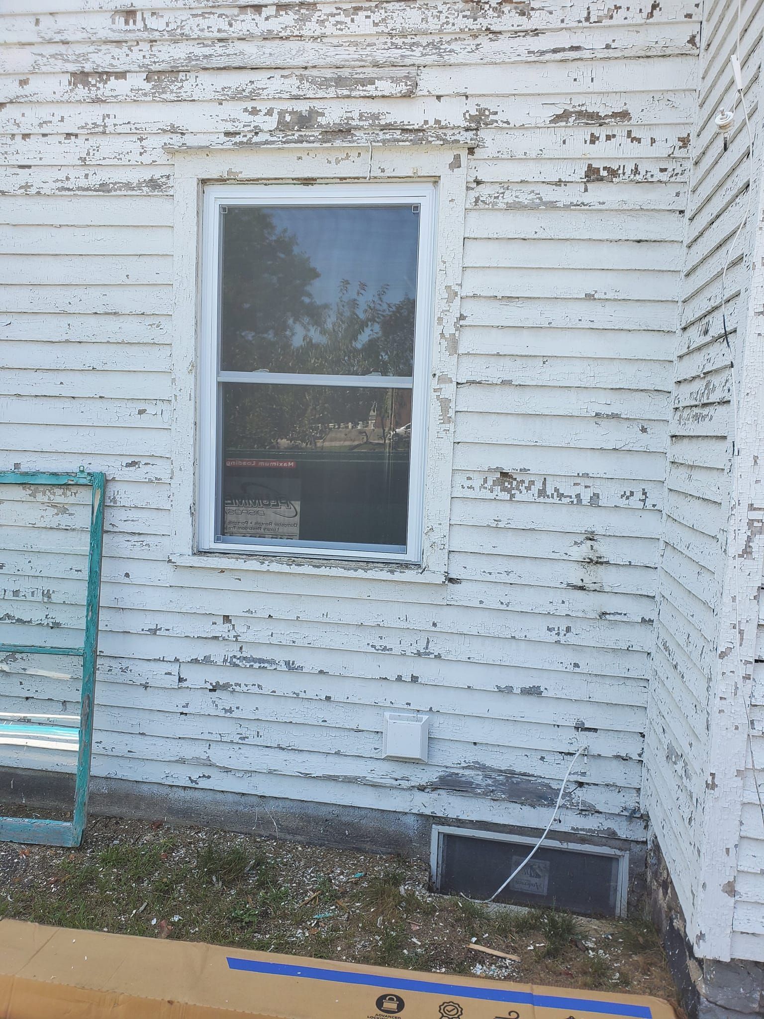 White weathered house wall with a small window and peeling paint, beside a concrete strip and green railing
