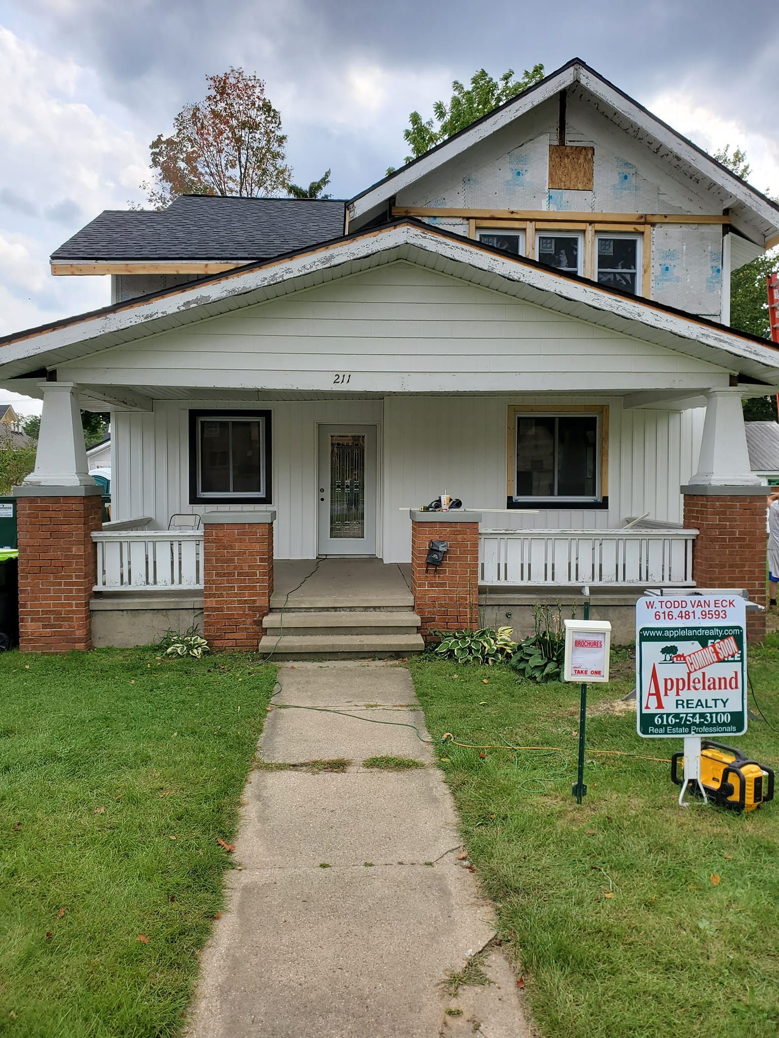 Small white bungalow with front porch, brick columns, lawn, and a real estate sign in front